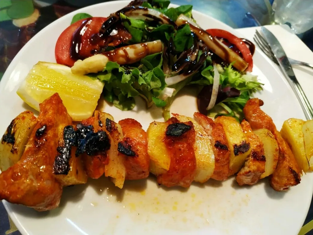 A skewer of grilled pieces beside a leafy salad and a lemon wedge on a plate