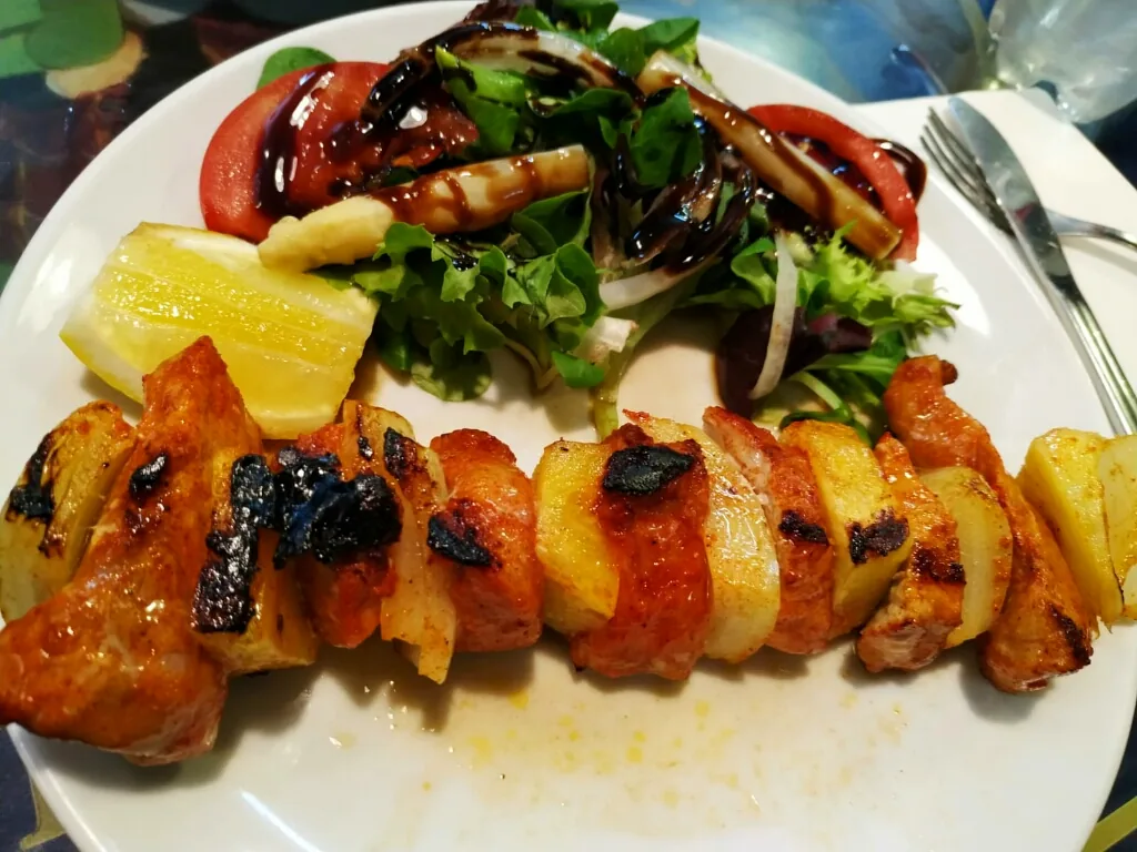 A grilled meat and vegetable skewer with pineapple and tomato salad