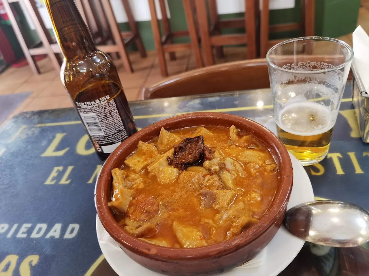 A clay bowl of meat and bread stew beside a glass of beer