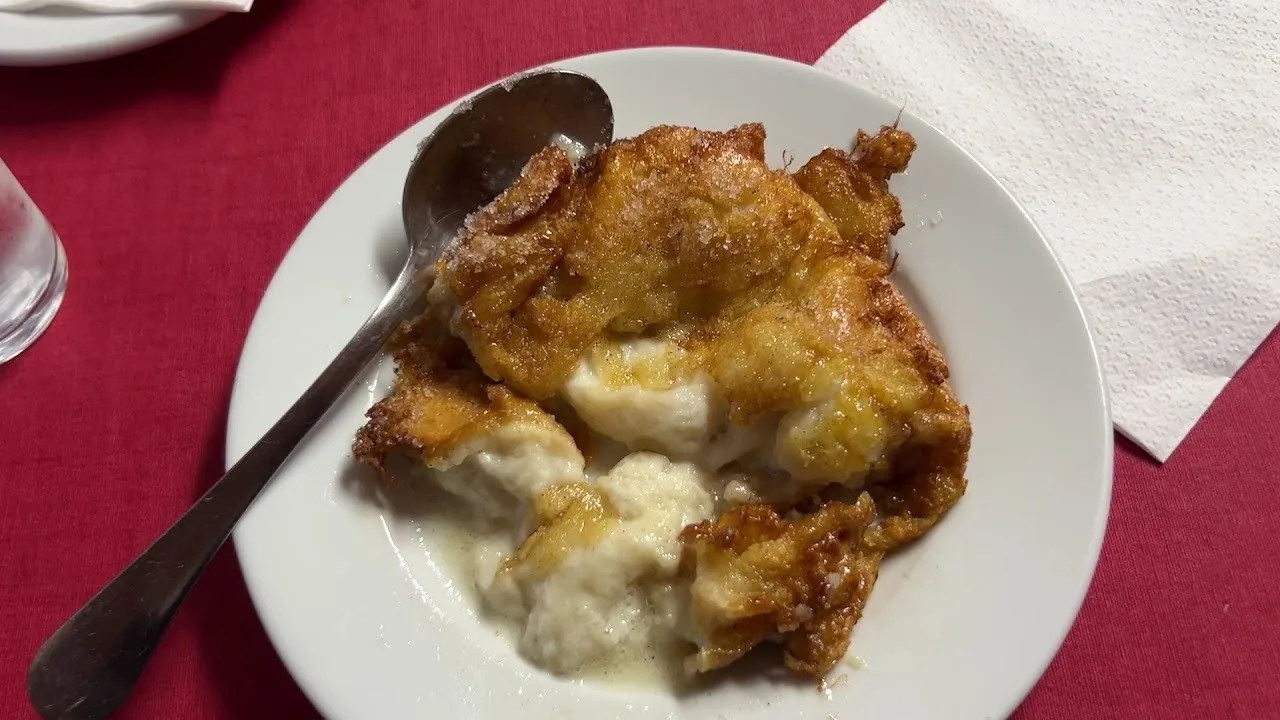 A golden fried torrija with sugar and a soft creamy centre on a white plate with a spoon