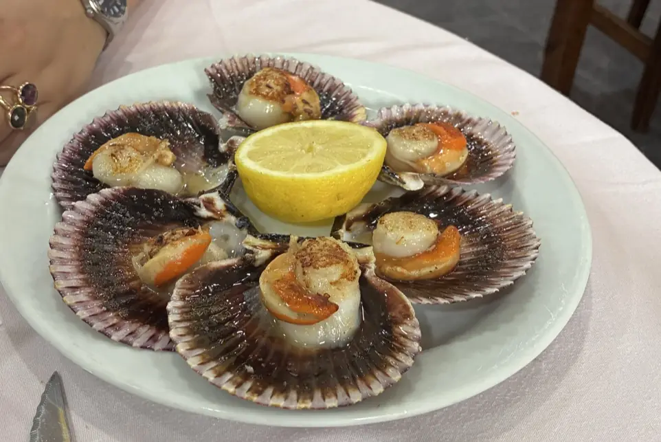 Grilled scallops in the shell arranged around a lemon half on a plate