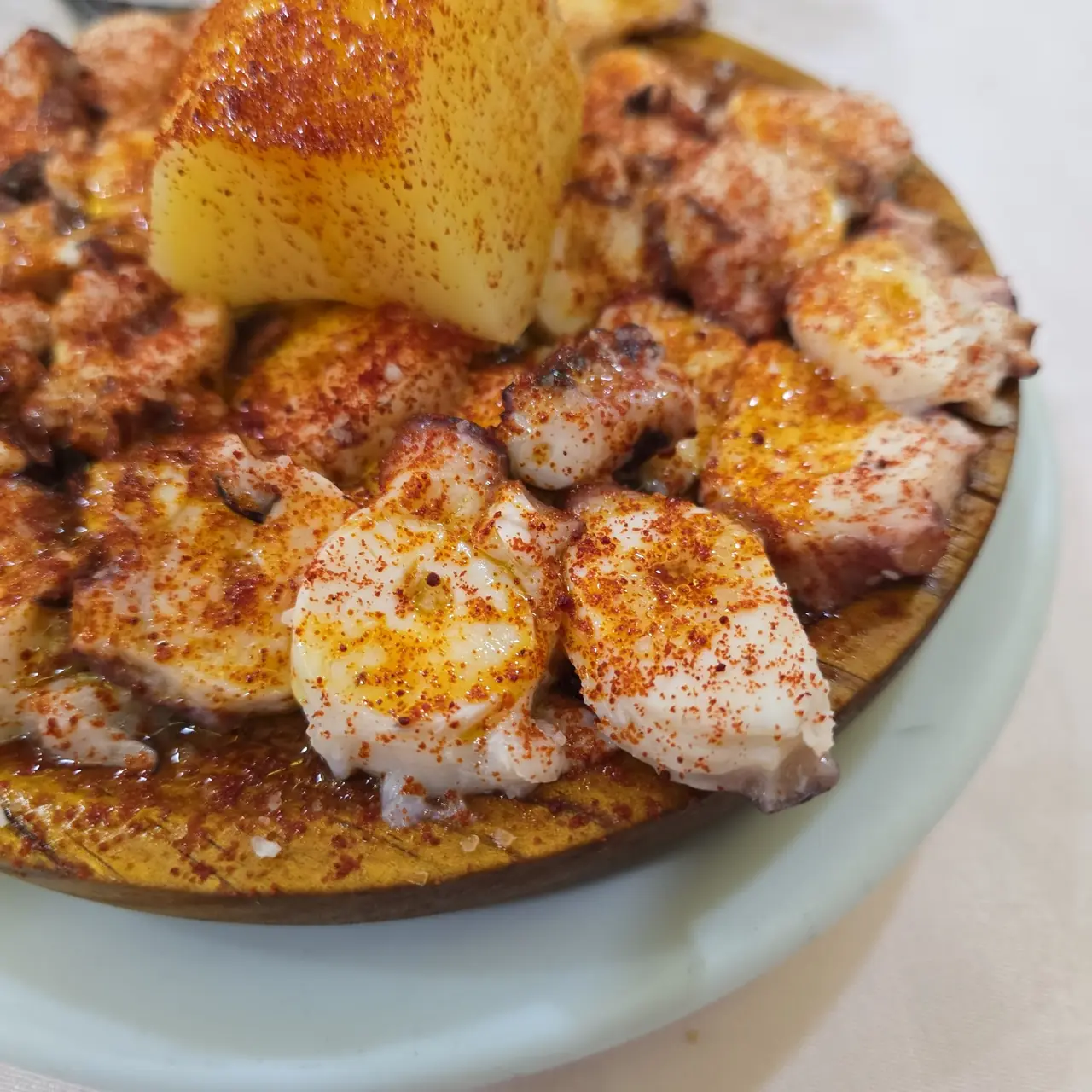 Octopus slices dusted with paprika alongside boiled potato on a wooden plate