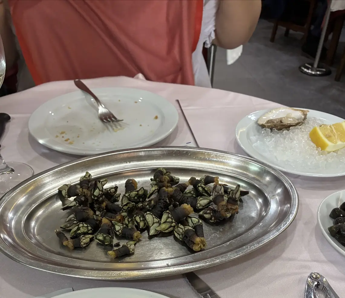 Goose barnacles served on a metal tray, with an oyster on ice in the background