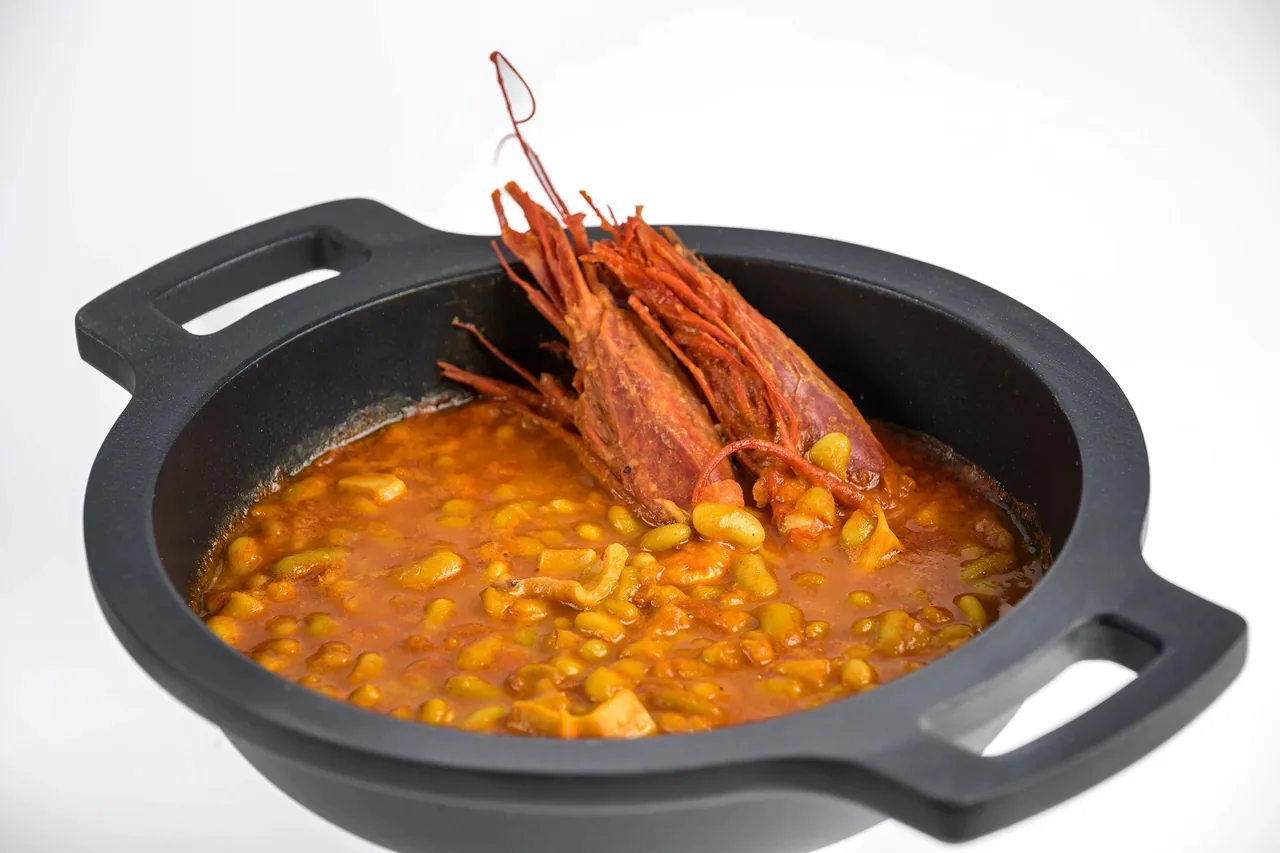 A black cast-iron pot of orange beans topped with a large red prawn