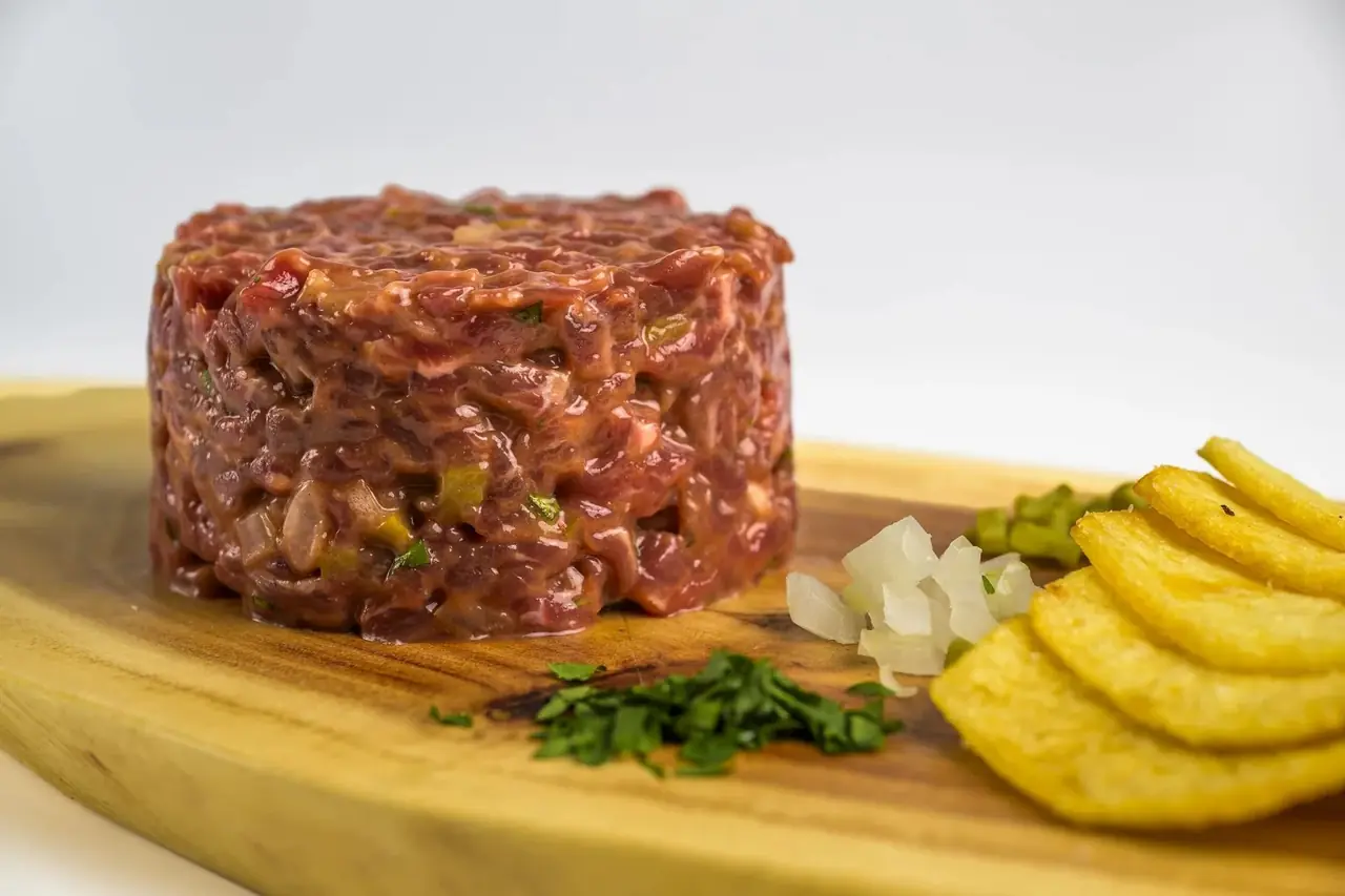 Steak tartare on a wooden board with chopped onion, parsley and crisps