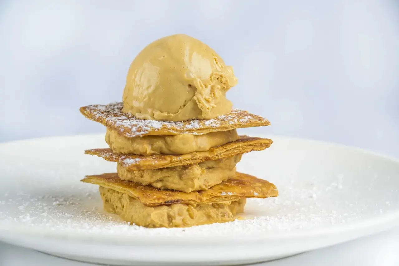 Layered mille-feuille dessert with a scoop of caramel ice cream and powdered sugar