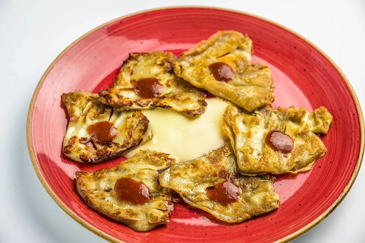 Six folded fried pieces with a dot of red sauce on a red plate beside a pool of pale cream