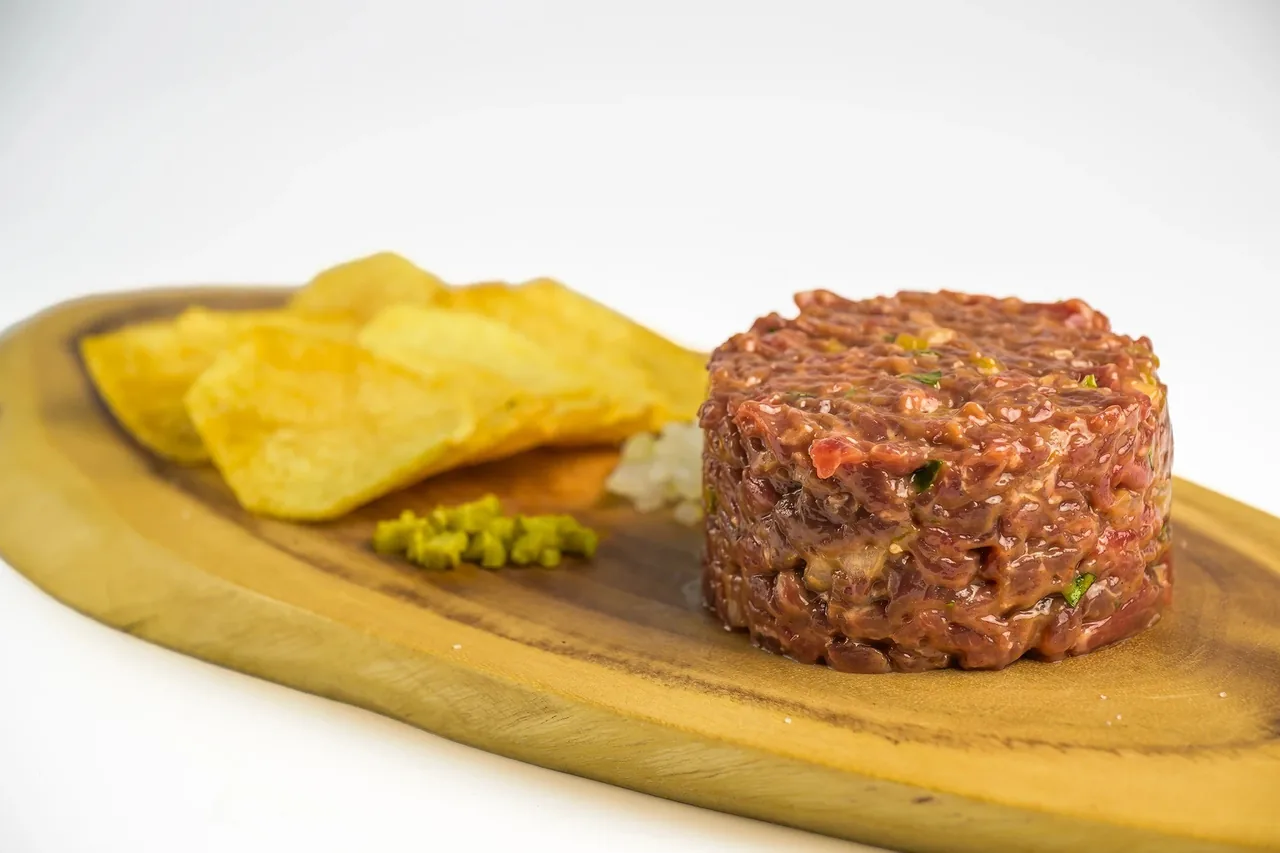 A round mound of chopped raw beef on a wooden board with potato chips