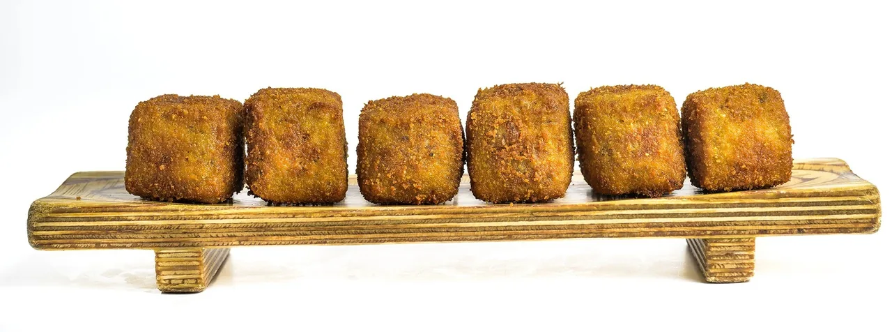 Six breaded croquettes lined up on a long wooden serving board