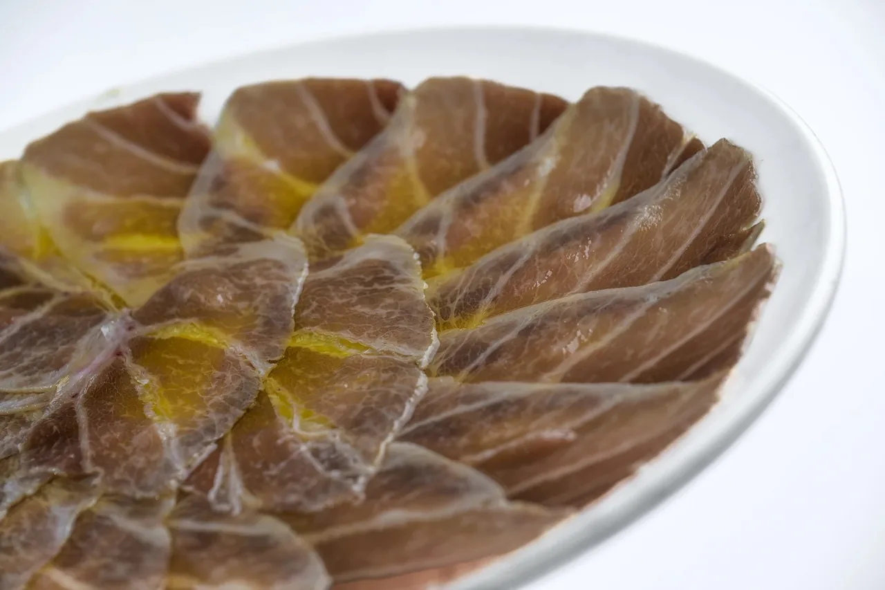 Thin slices of cured meat drizzled with olive oil on a white plate