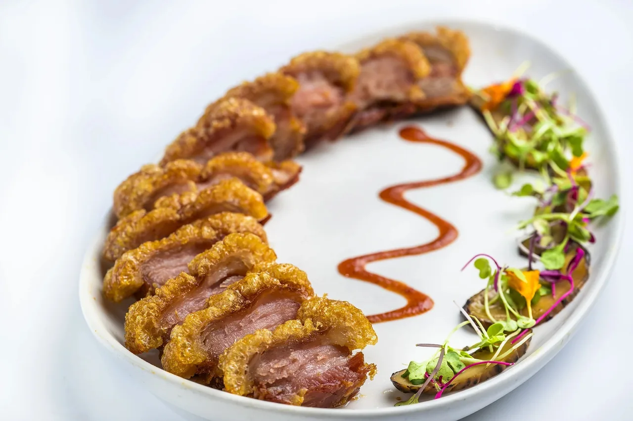 Sliced crisp-crusted meat arranged in a curve on a white plate with sauce and small leaves
