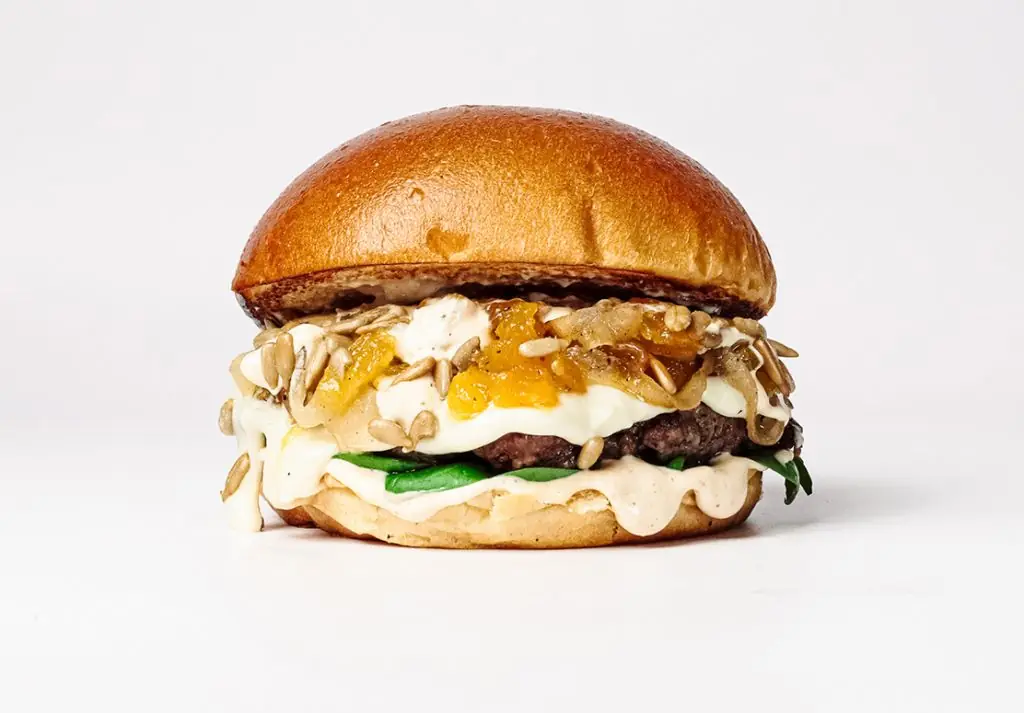 Smashed burger with melted white cheese, sunflower seeds, caramelized onion, and creamy sauce on a toasted brioche bun, La Central Burgers