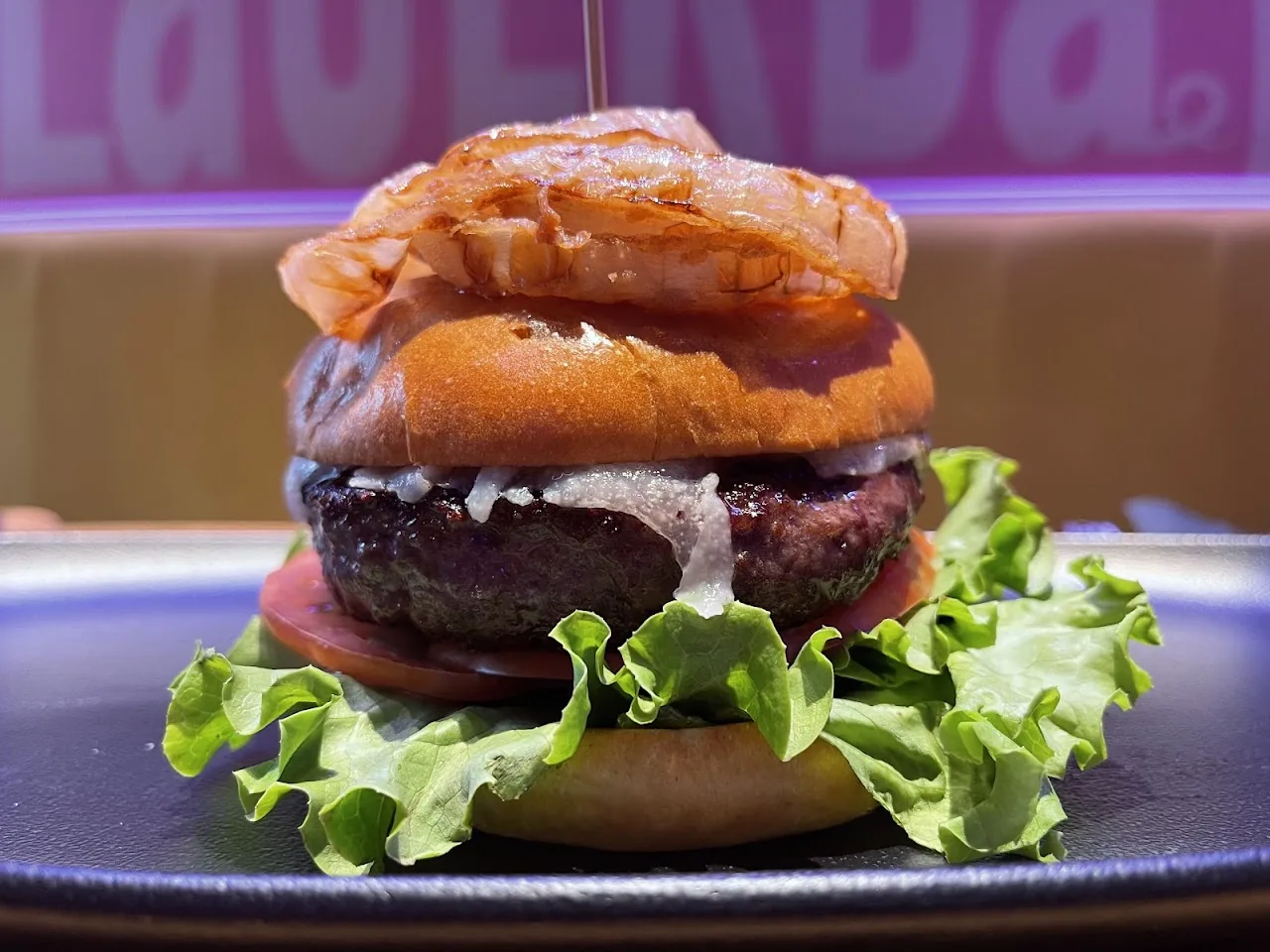 A stacked burger with onion rings and lettuce on a dark plate