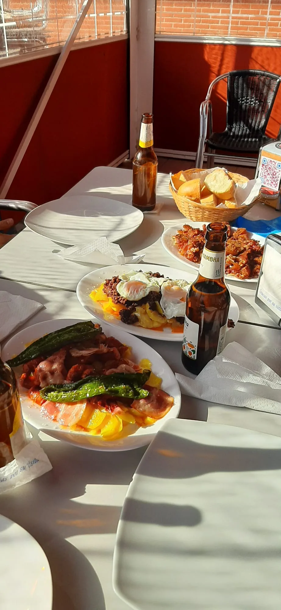 A table spread with grilled meat and green peppers, fried eggs over potatoes, and a bread basket
