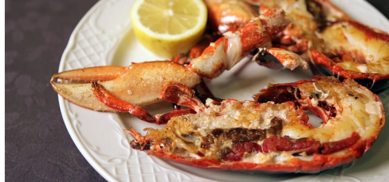 A cooked lobster on a white plate with a lemon wedge