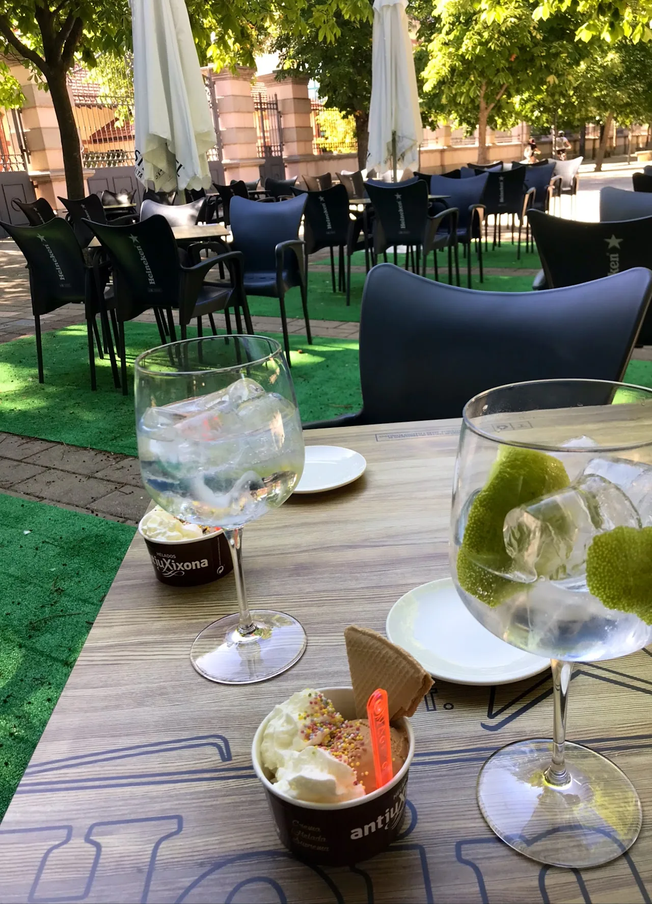 Two gin and tonic cocktails with lime and mint on an outdoor table, with a small ice cream cup