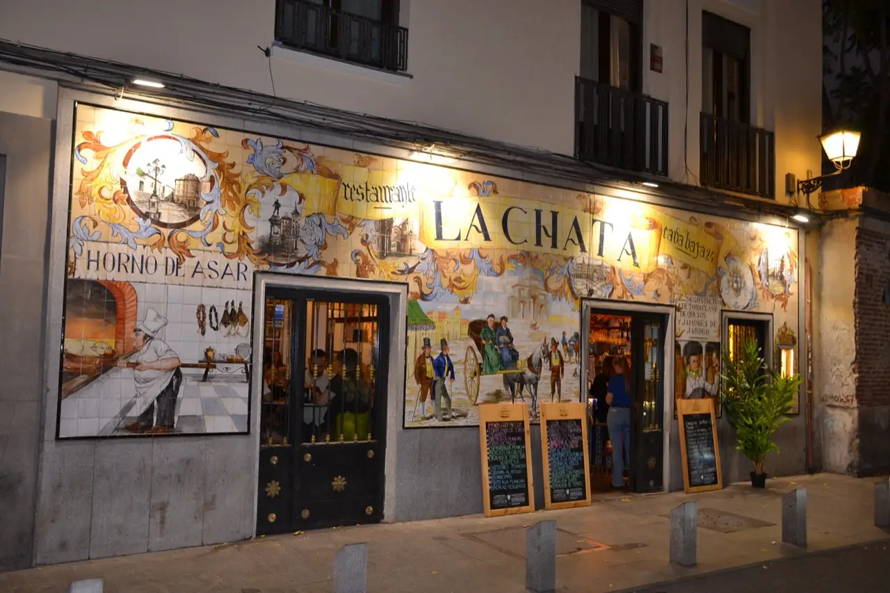 Nighttime exterior of La Chata's tiled facade at an angle, with staff and customers visible through the open doorway.