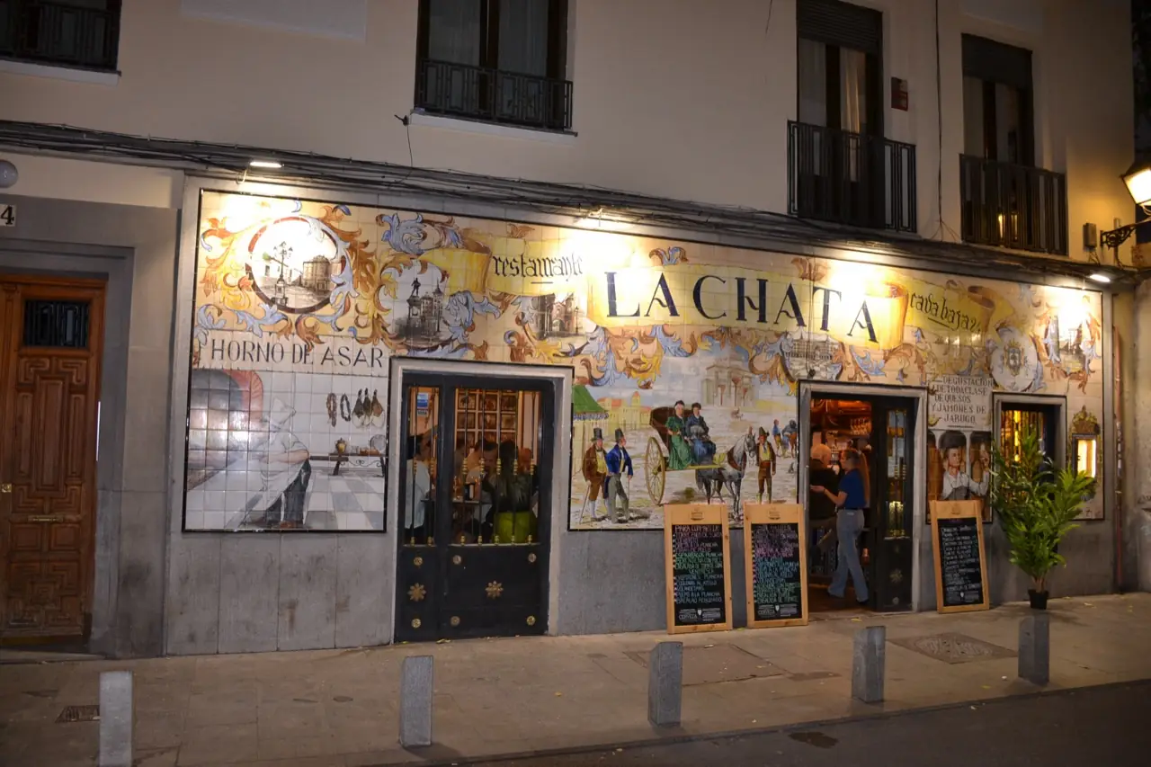 Nighttime exterior of La Chata's tiled facade, a woman standing in the lit doorway.