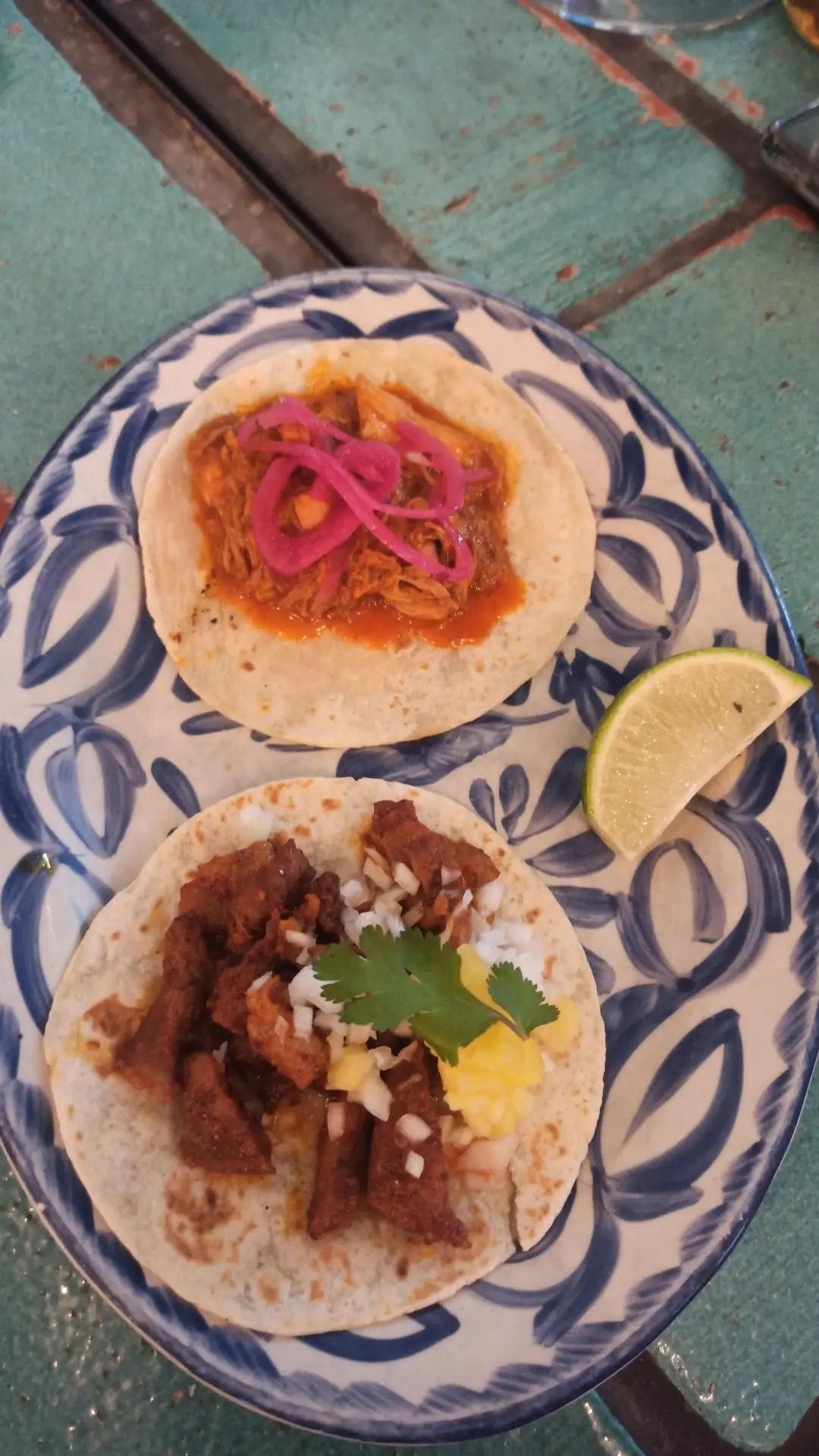 Two tacos with pickled red onion on a decorative blue-and-white plate