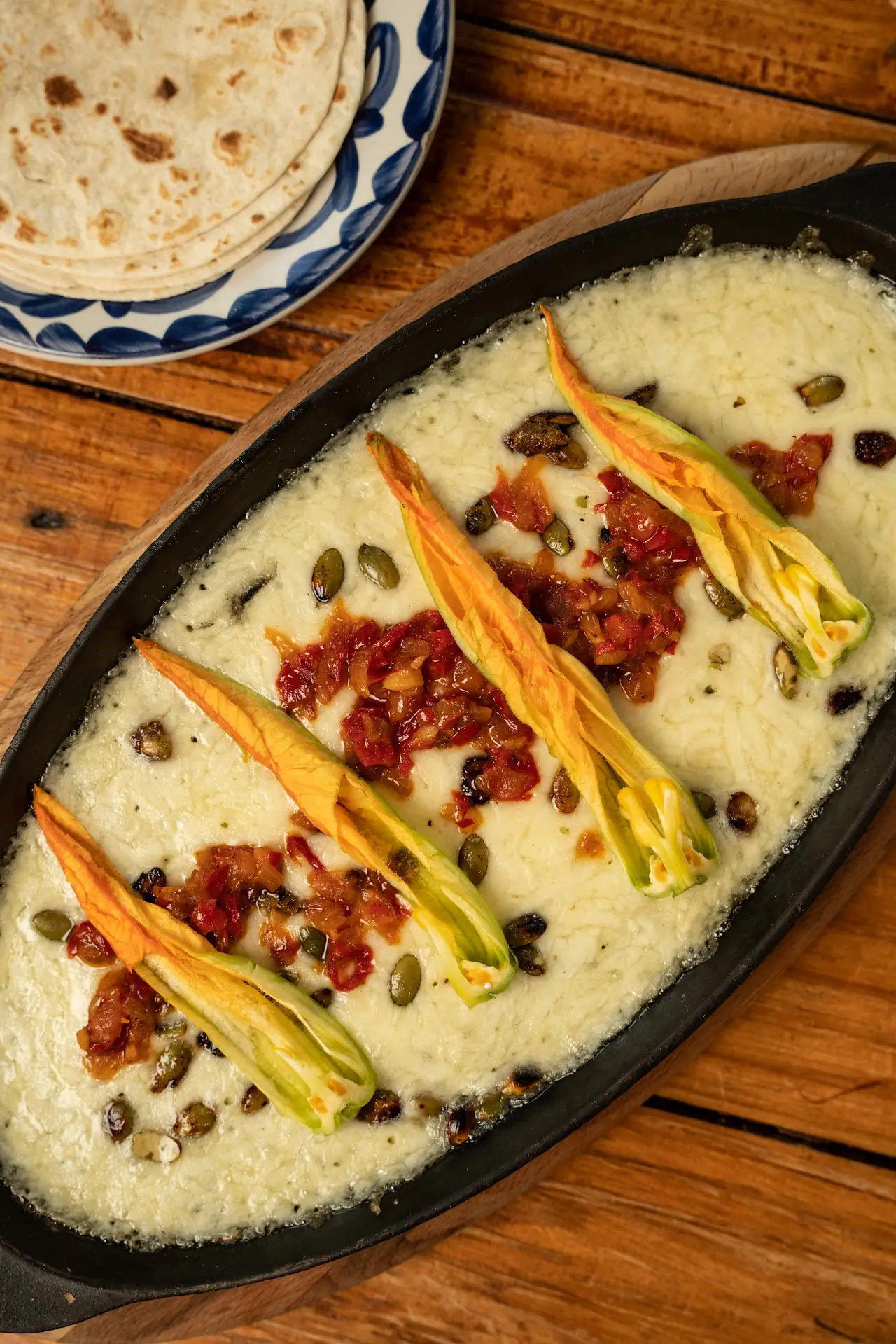 Squash blossoms over melted cheese with diced tomato on an oval platter