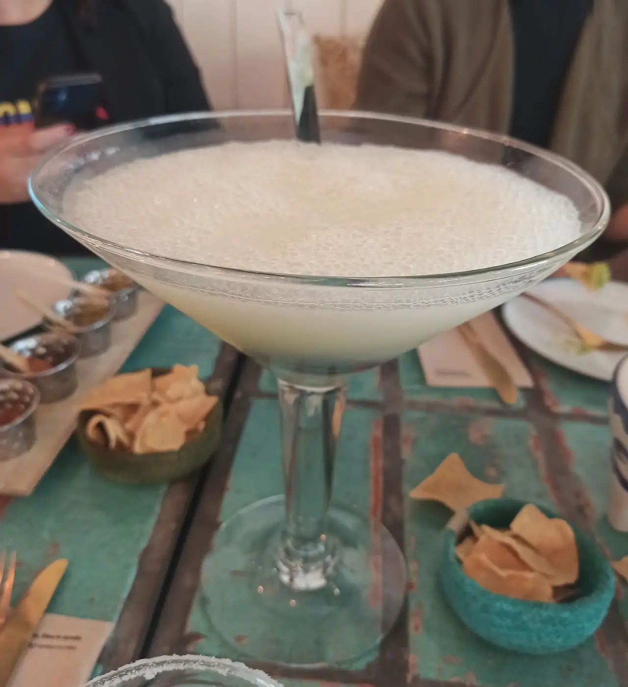 A frothy margarita in a coupe glass on a turquoise table