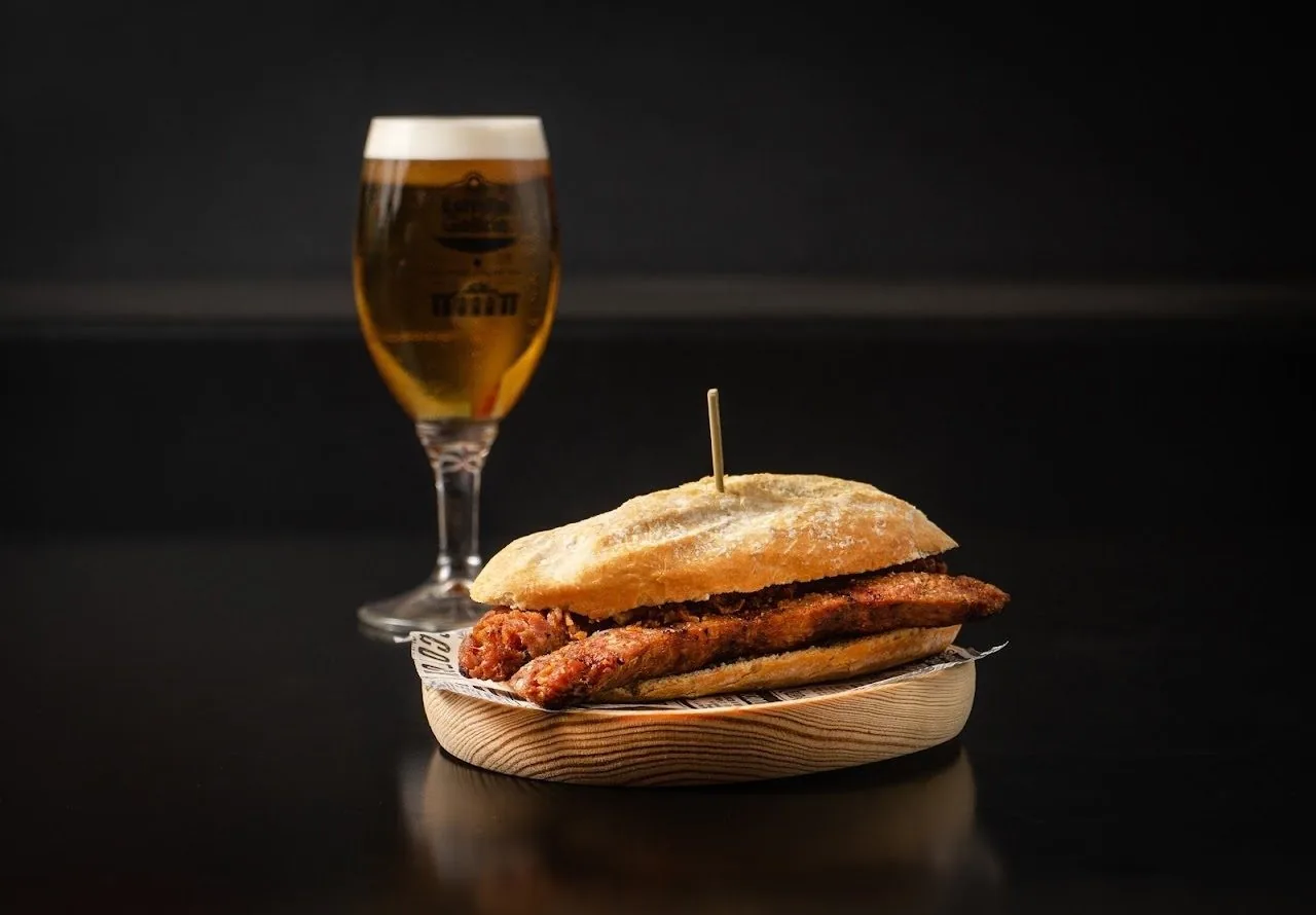 A sausage sandwich in a crusty roll next to a glass of beer