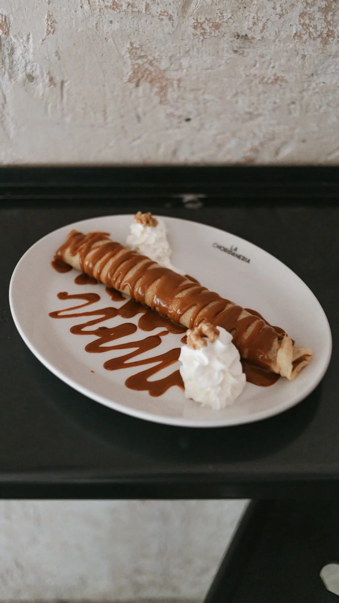 A rolled pancake with caramel sauce and whipped cream on a white plate