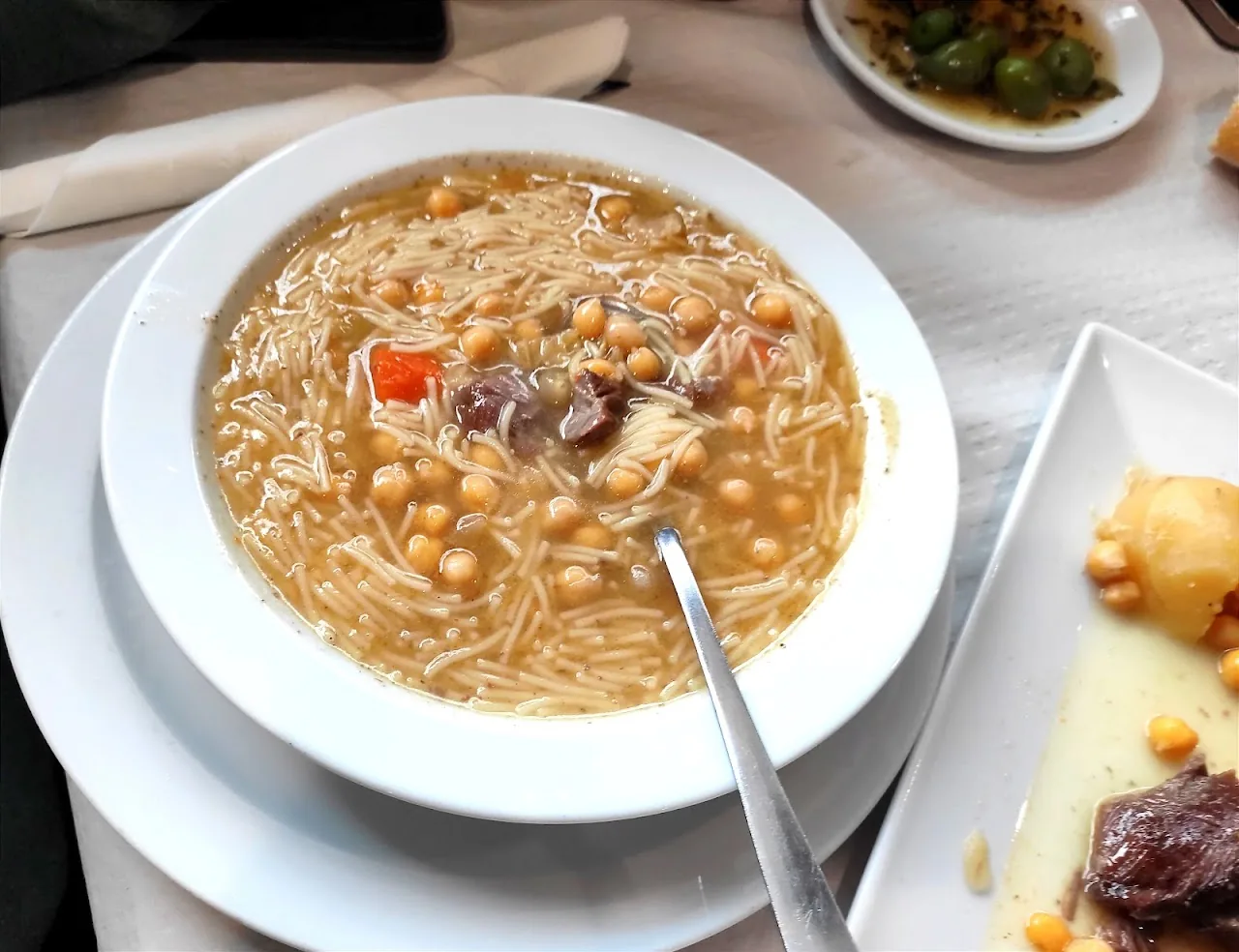 A bowl of cocido stew with chickpeas, meat, and noodles