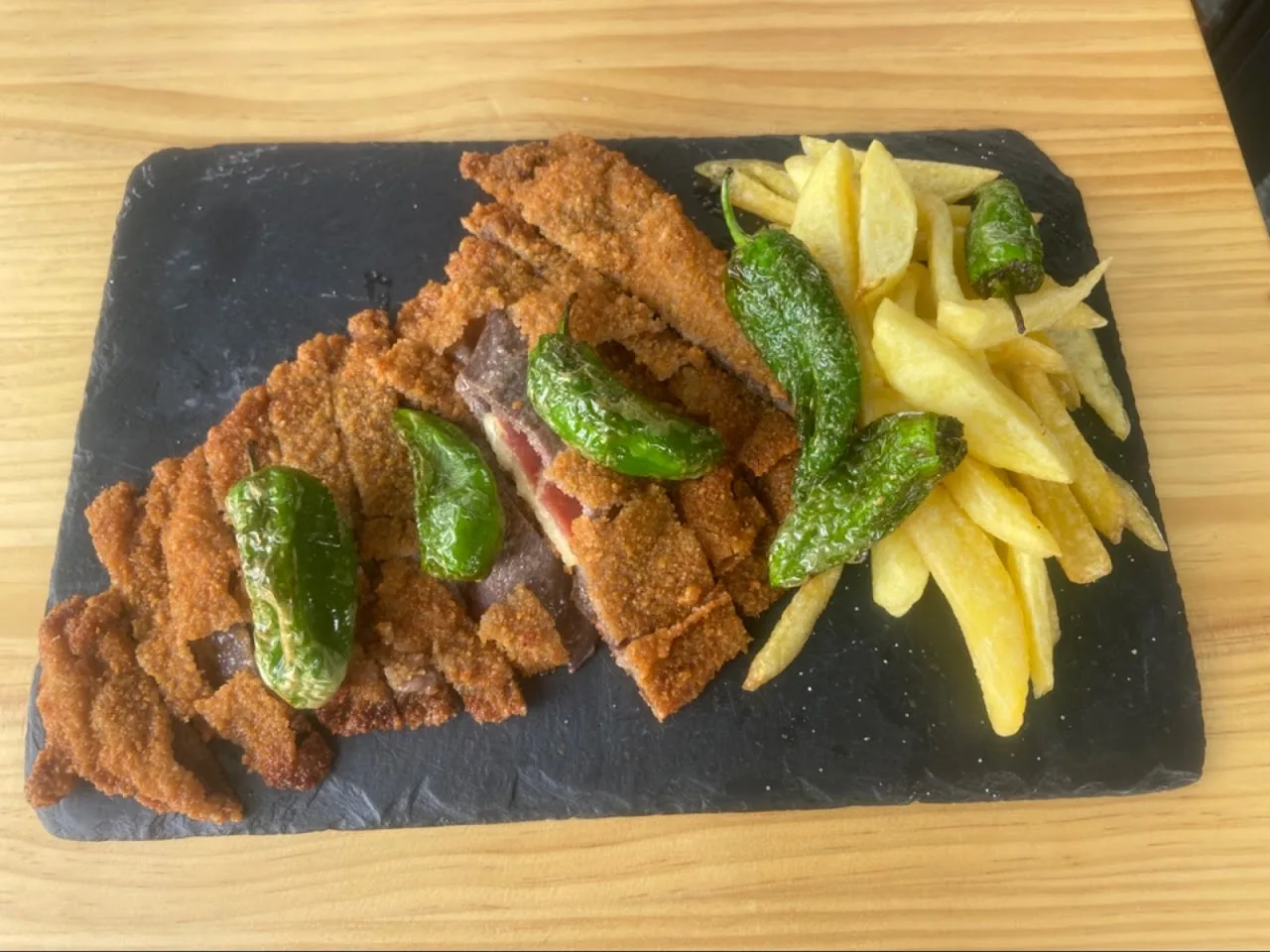 A breaded veal cutlet with fried green peppers and french fries