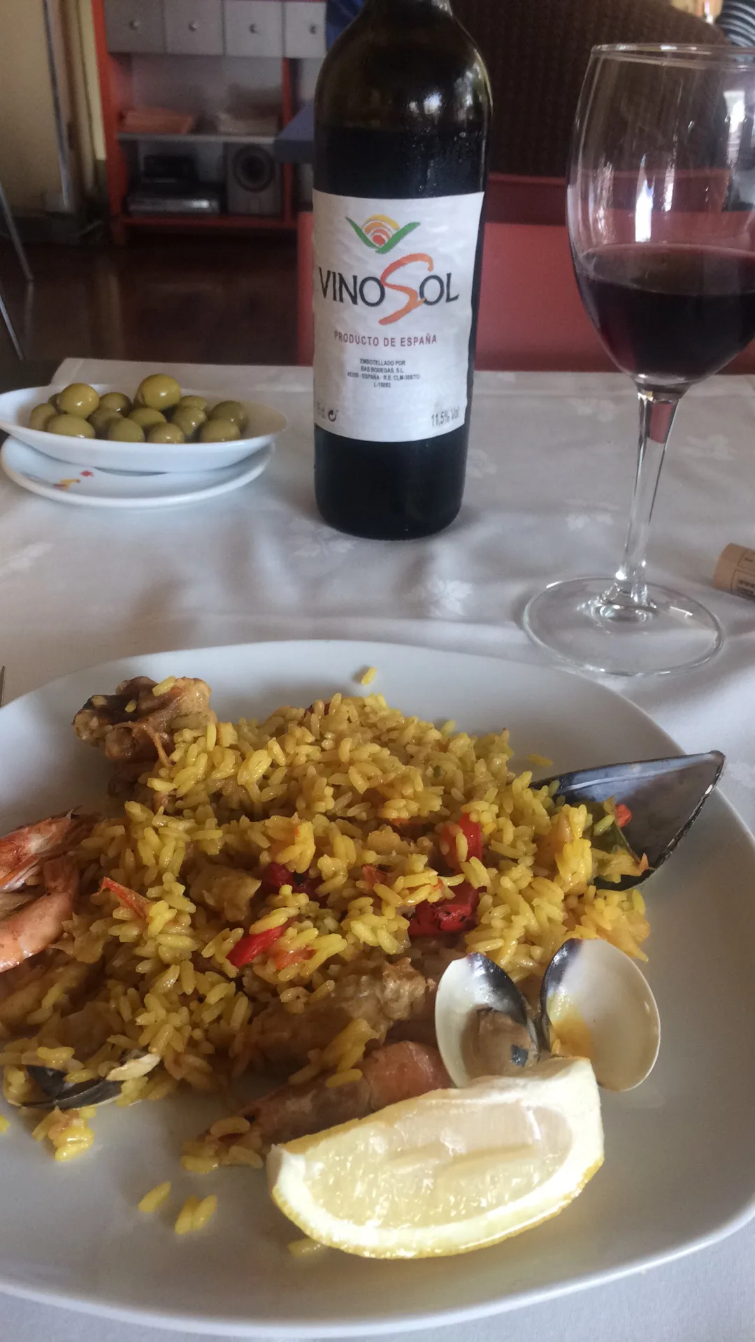 A plate of paella with mussels and a lemon wedge, beside a glass of red wine