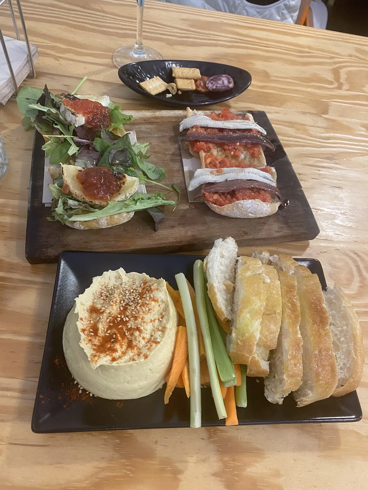 An overhead spread of tapas toasts, a bowl of dip with bread, and a small salad