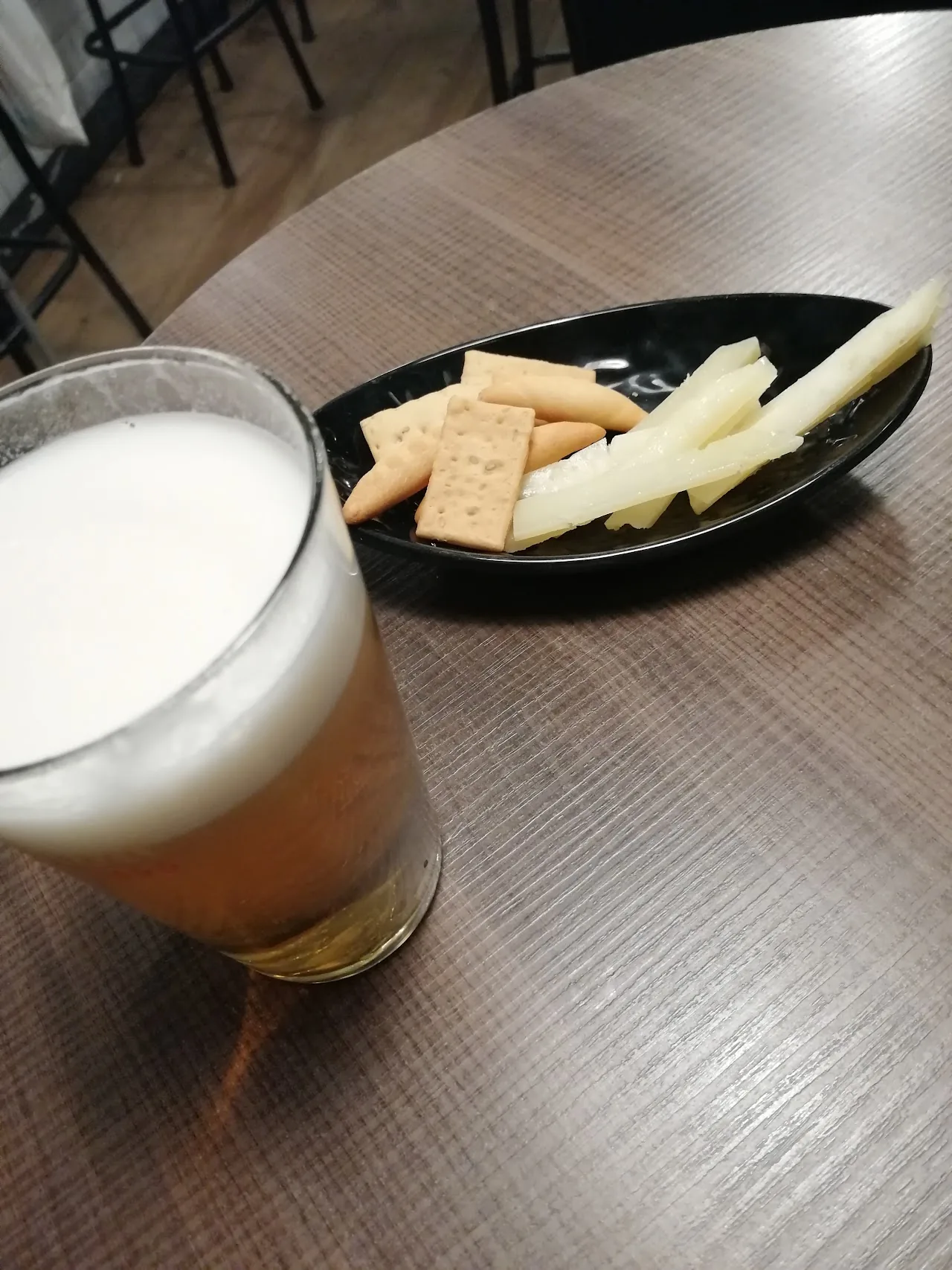 A glass of beer beside a plate of crackers and cheese