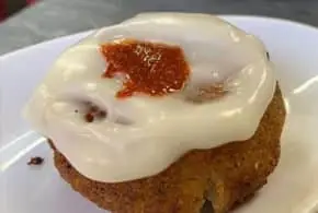 A fried potato croquette-style bomba topped with white aioli and a dab of spicy red sauce, on a white plate at La Cova Fumada.