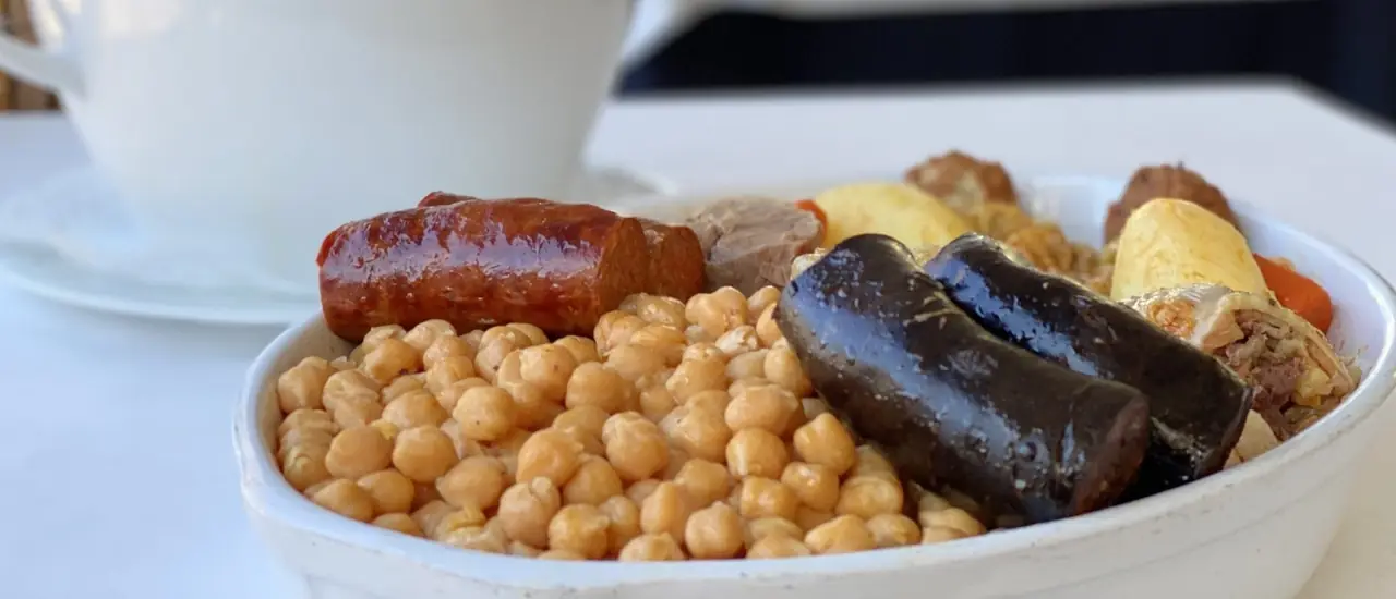 A white dish of chickpeas with chorizo, morcilla and boiled meats
