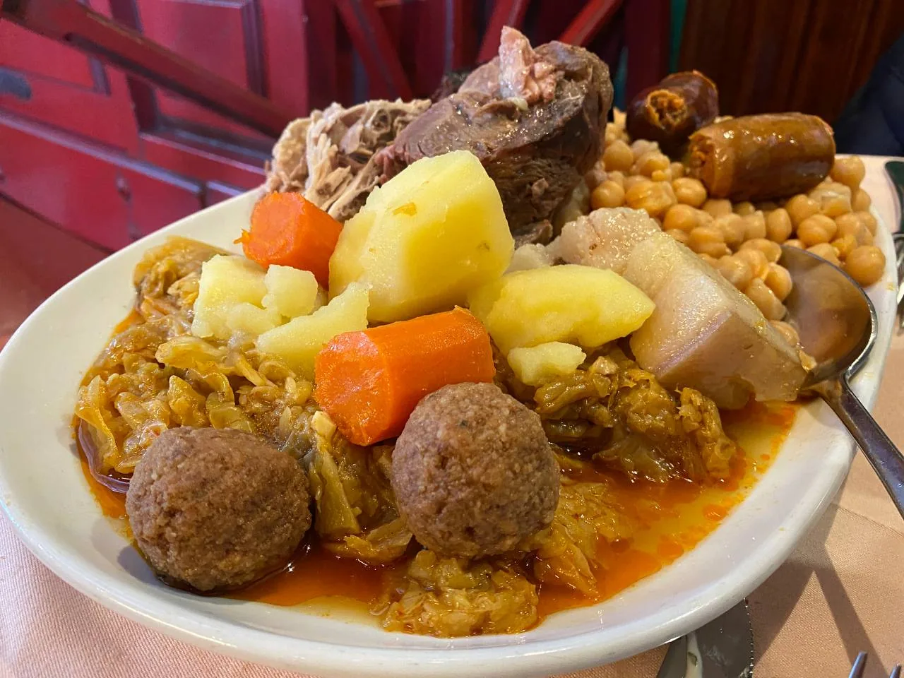 A plate of cocido madrileño with meat, potatoes, and chickpeas