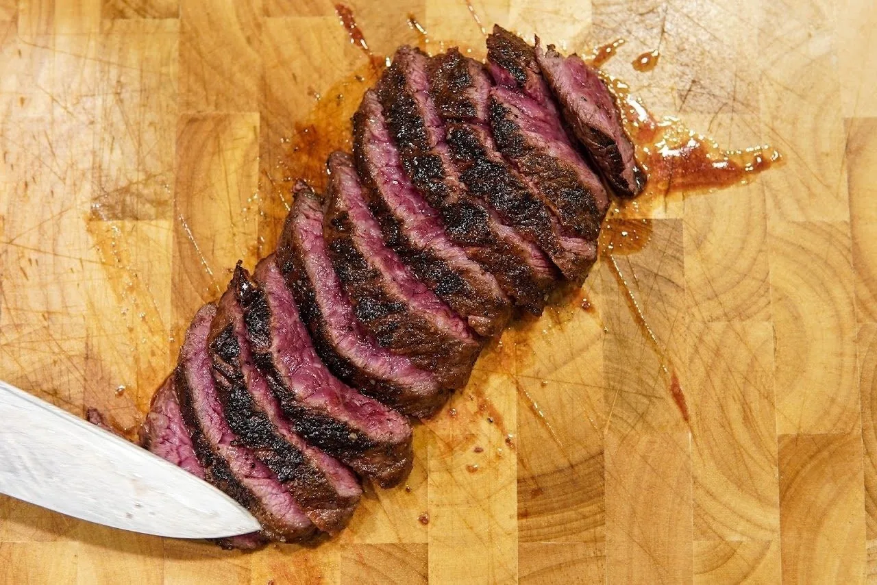 Thin slices of seared steak fanned out on a wooden board beside a knife