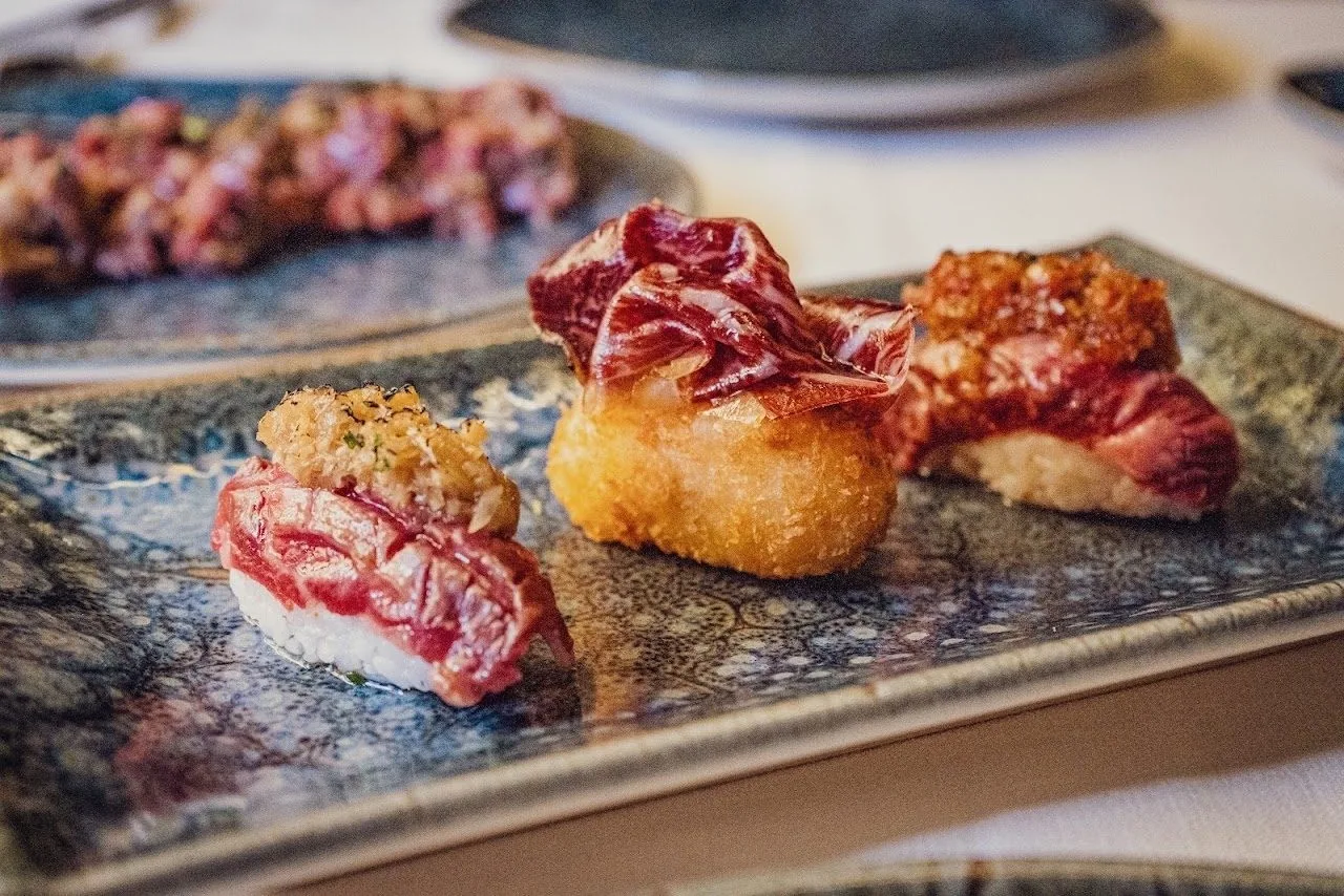 Two small plated bites of meat on a rectangular blue-grey plate