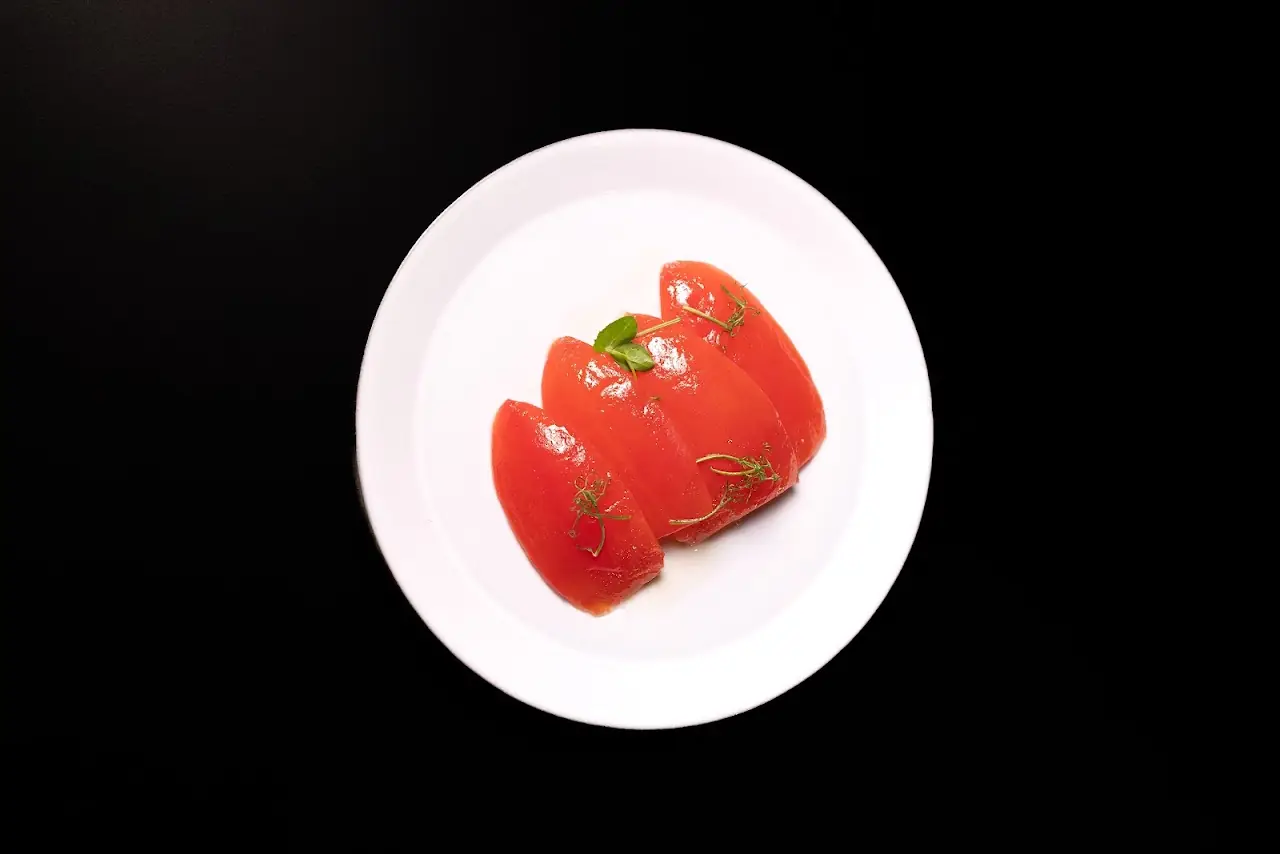 Sliced tomato wedges on a white plate against a black background