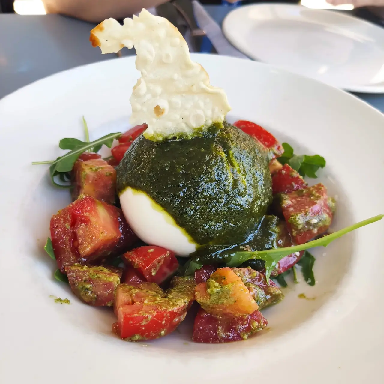 Burrata topped with pesto over diced tomatoes and arugula