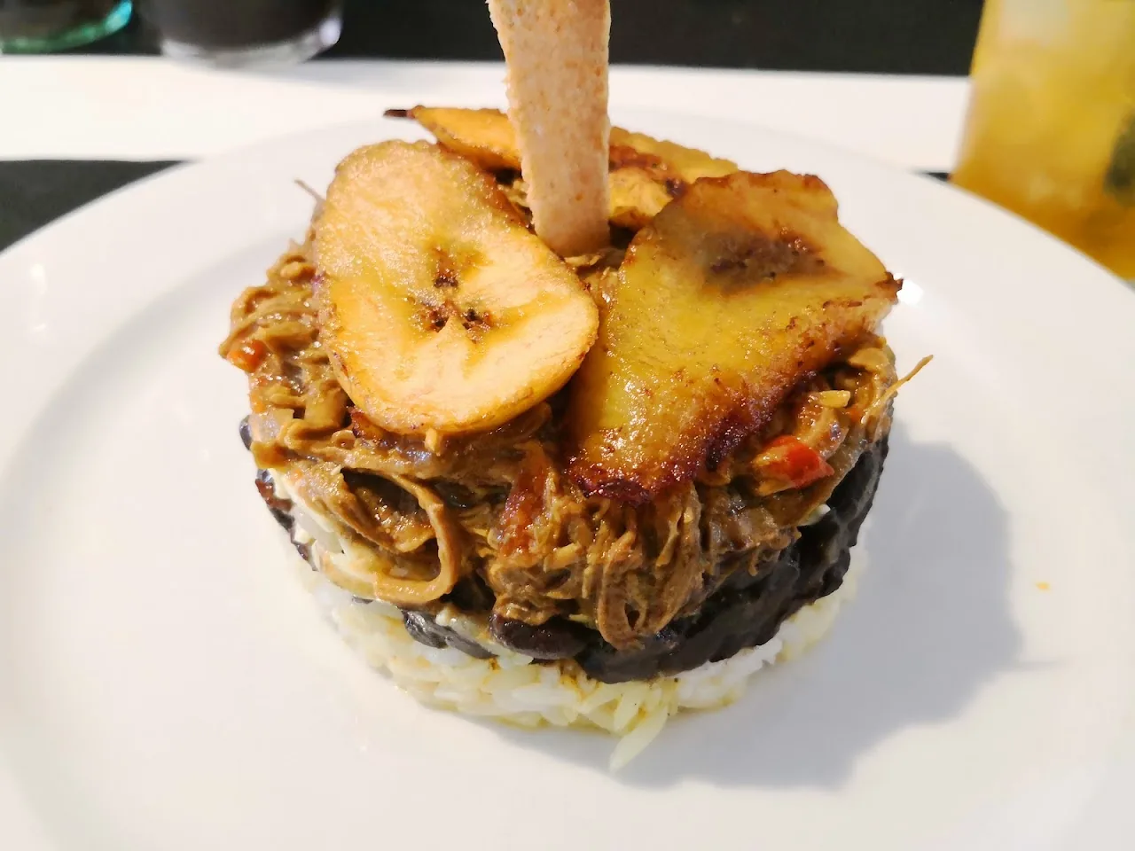 A stacked cachapa (corn cake) topped with pulled meat and grilled plantains