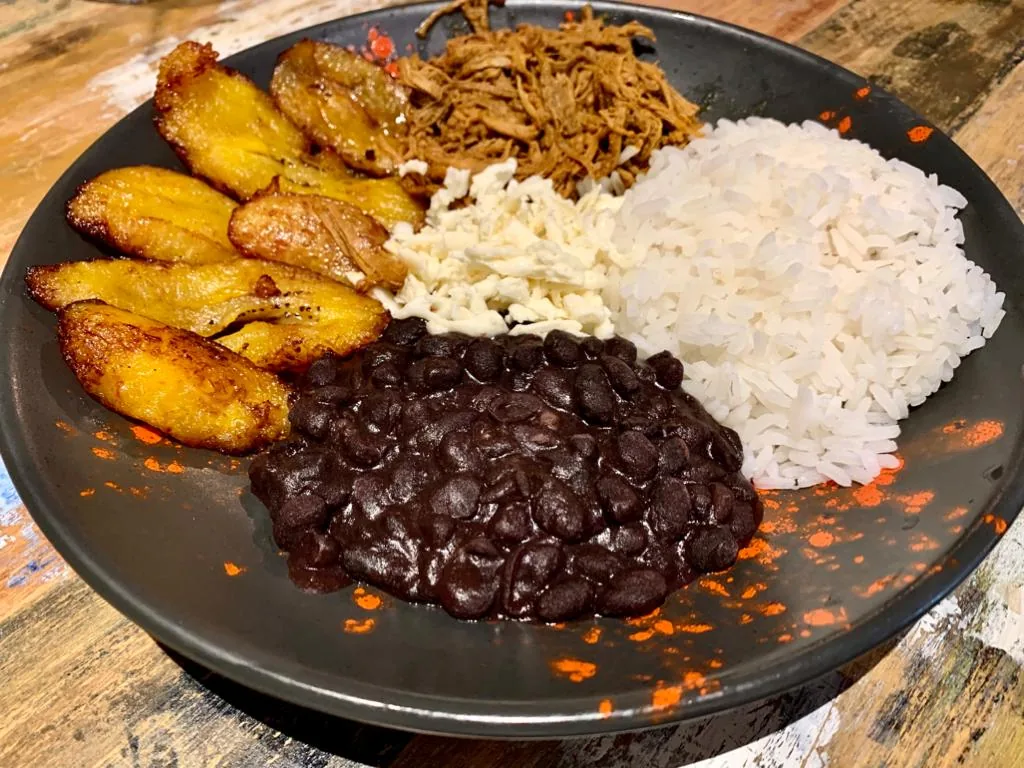 A plate of pabellon criollo with black beans, rice, shredded beef, and fried plantains