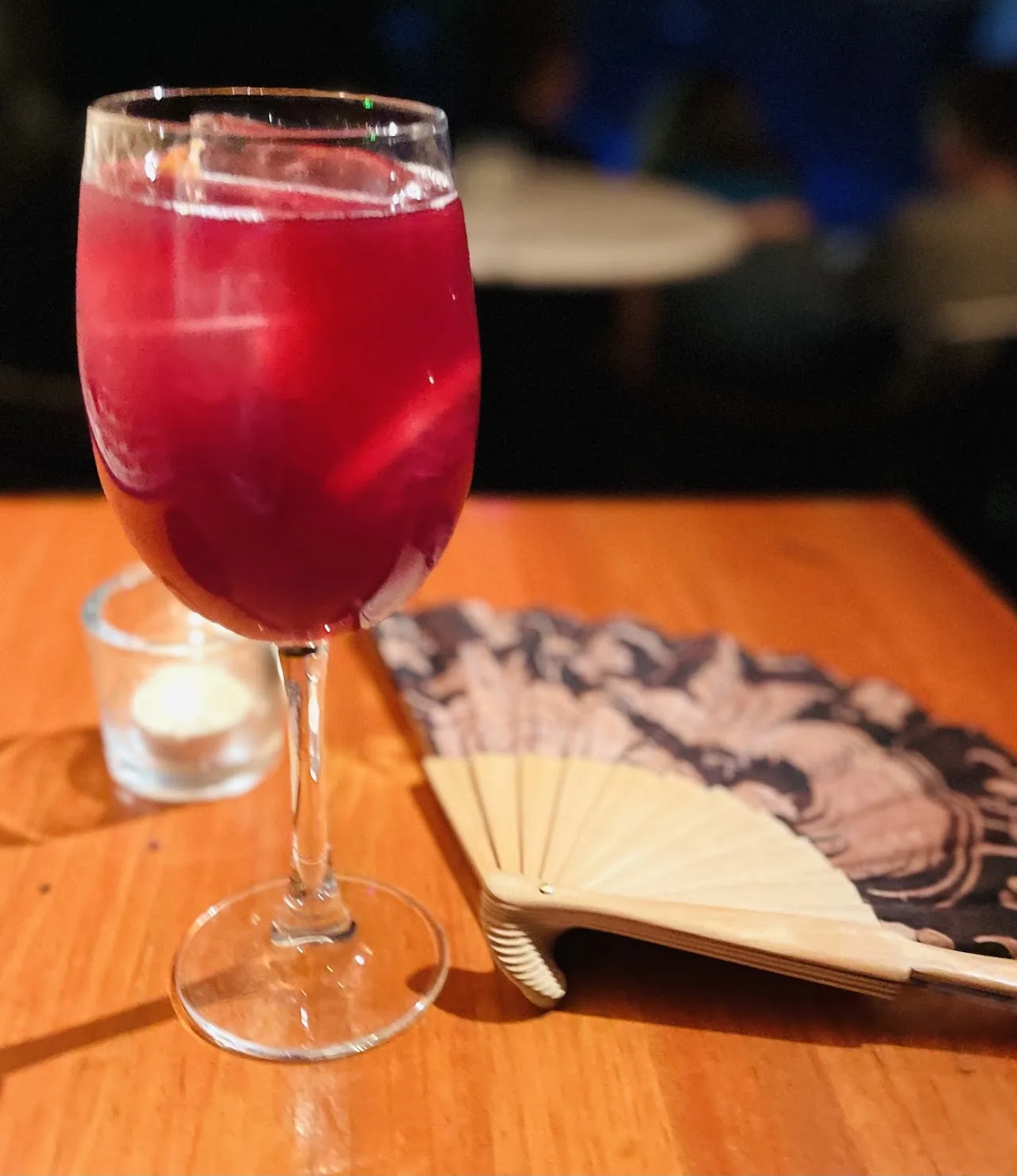 A glass of red sangria on a table with a folding fan