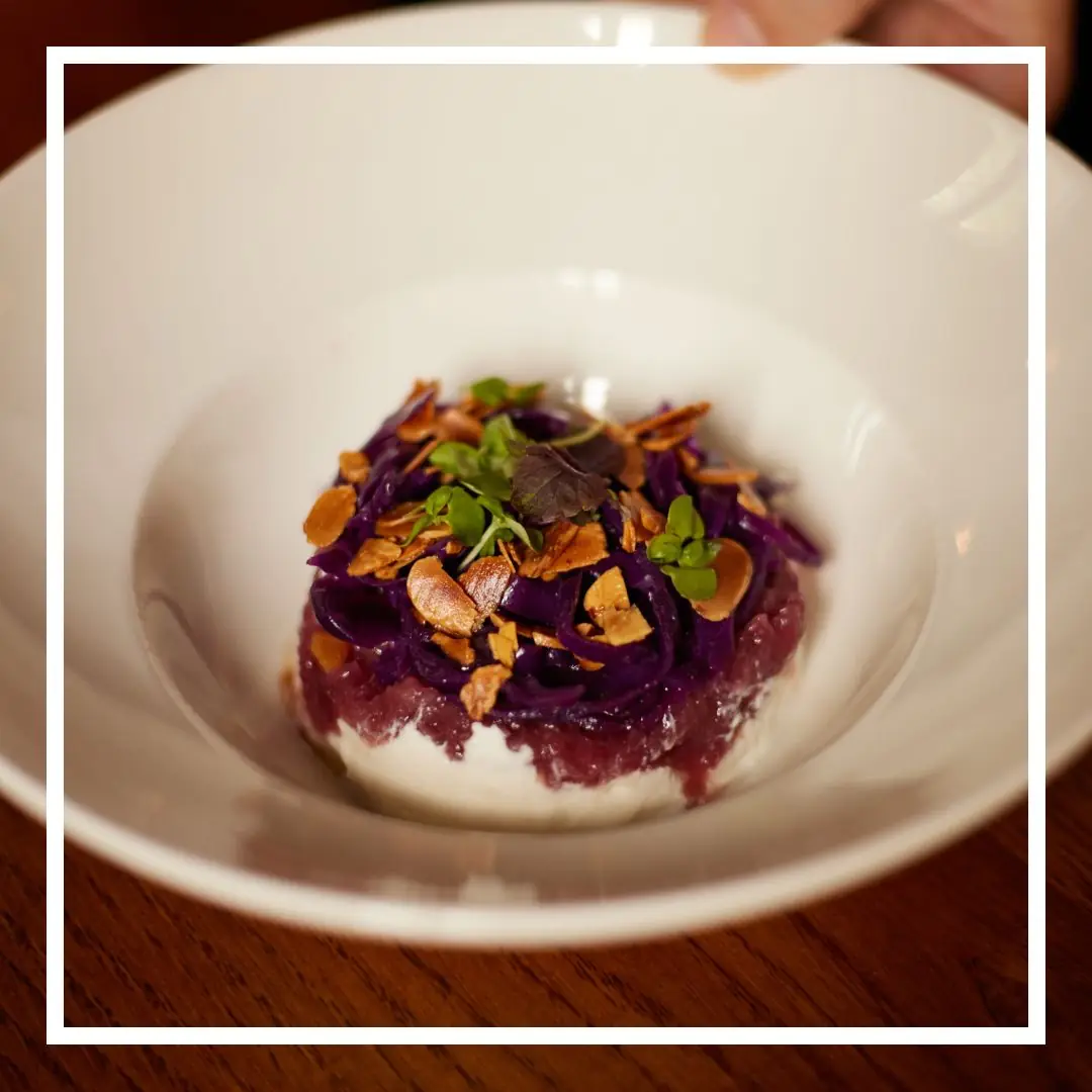 Tartare topped with shredded purple cabbage and toasted almond flakes in a white bowl, at La Dama