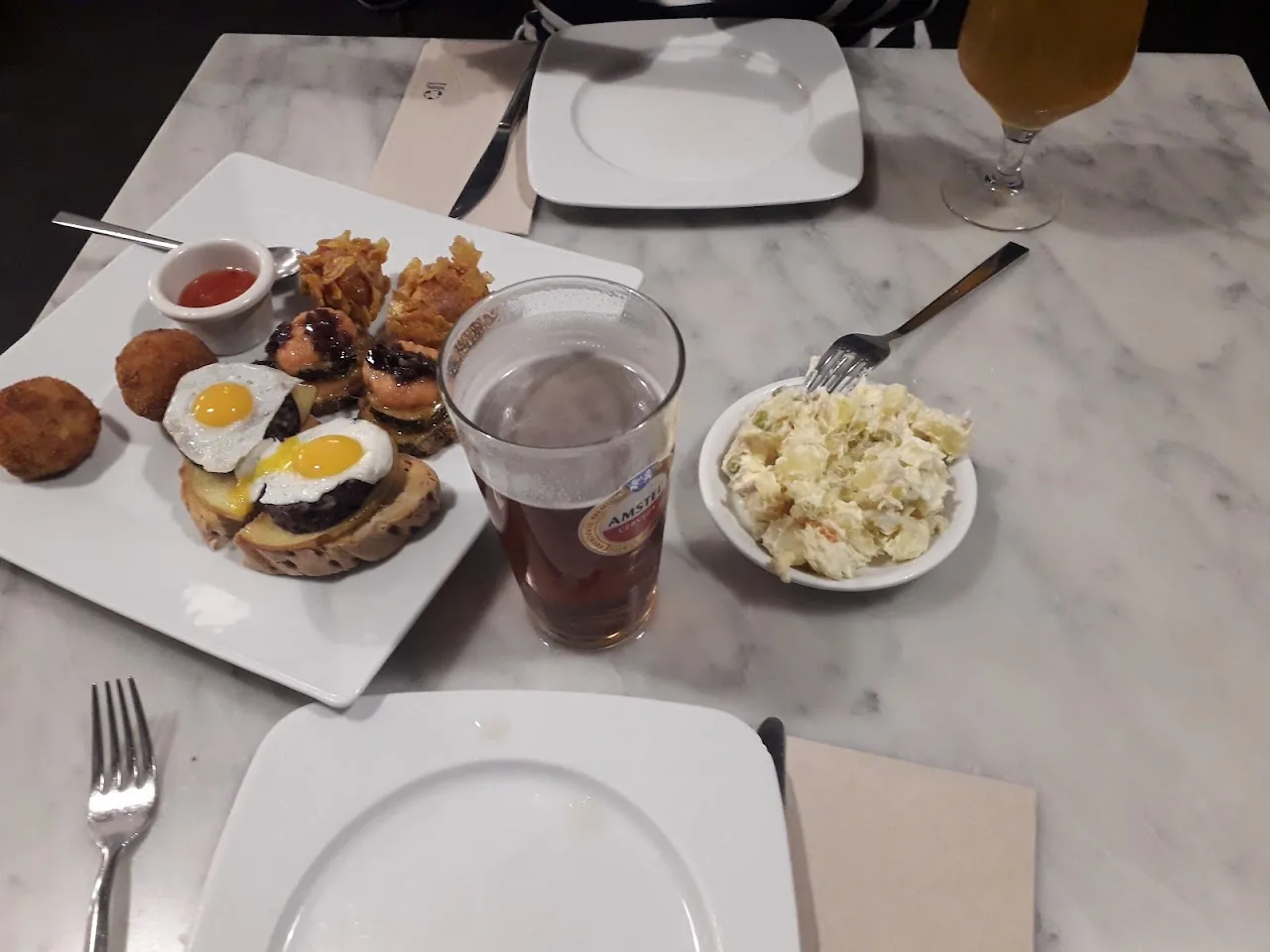 A table spread of tostas, fried croquettes, olives, and a cold drink