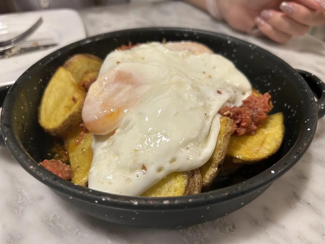 A fried egg over potatoes with chorizo in a black dish