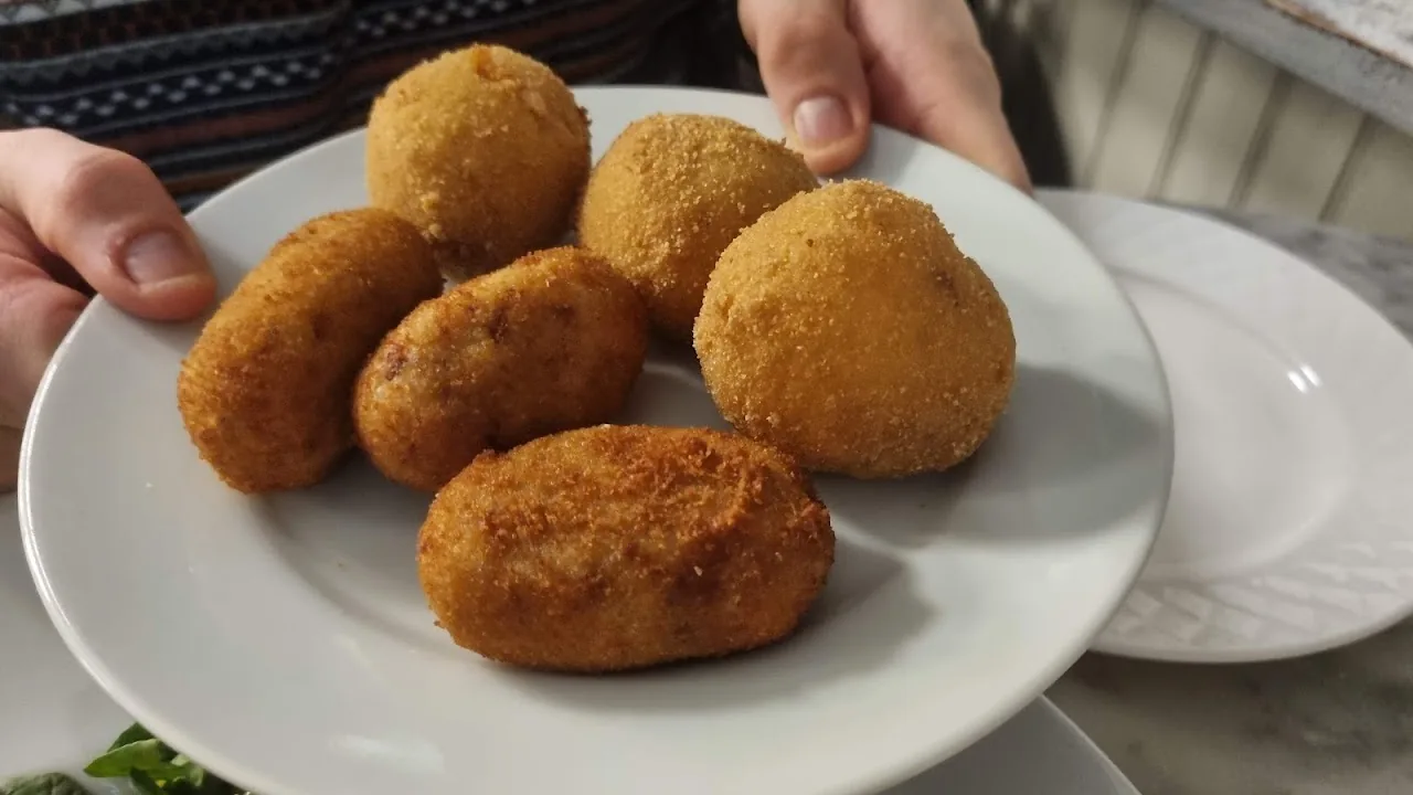 A hand presenting a plate of fried croquettes