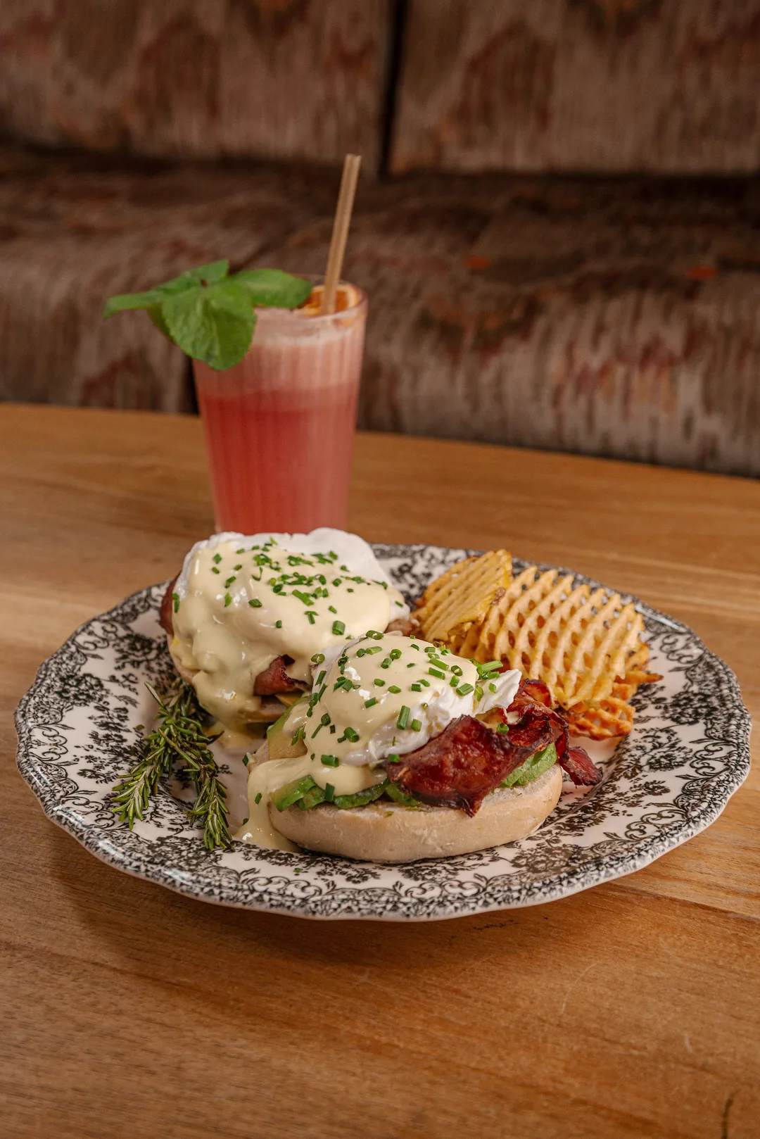 An eggs Benedict-style dish with crispy potatoes and a pink smoothie