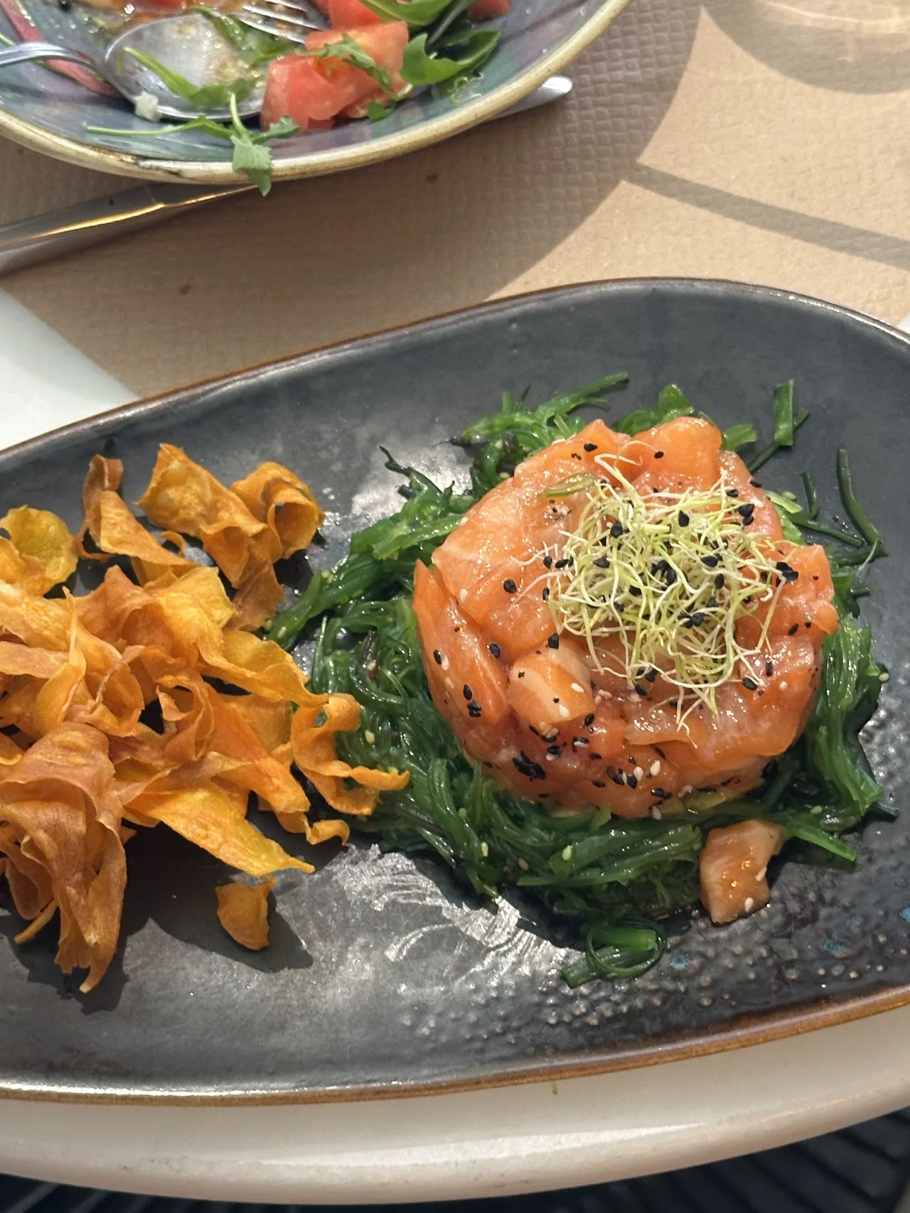 A salmon dish over greens with shredded carrot on a dark plate