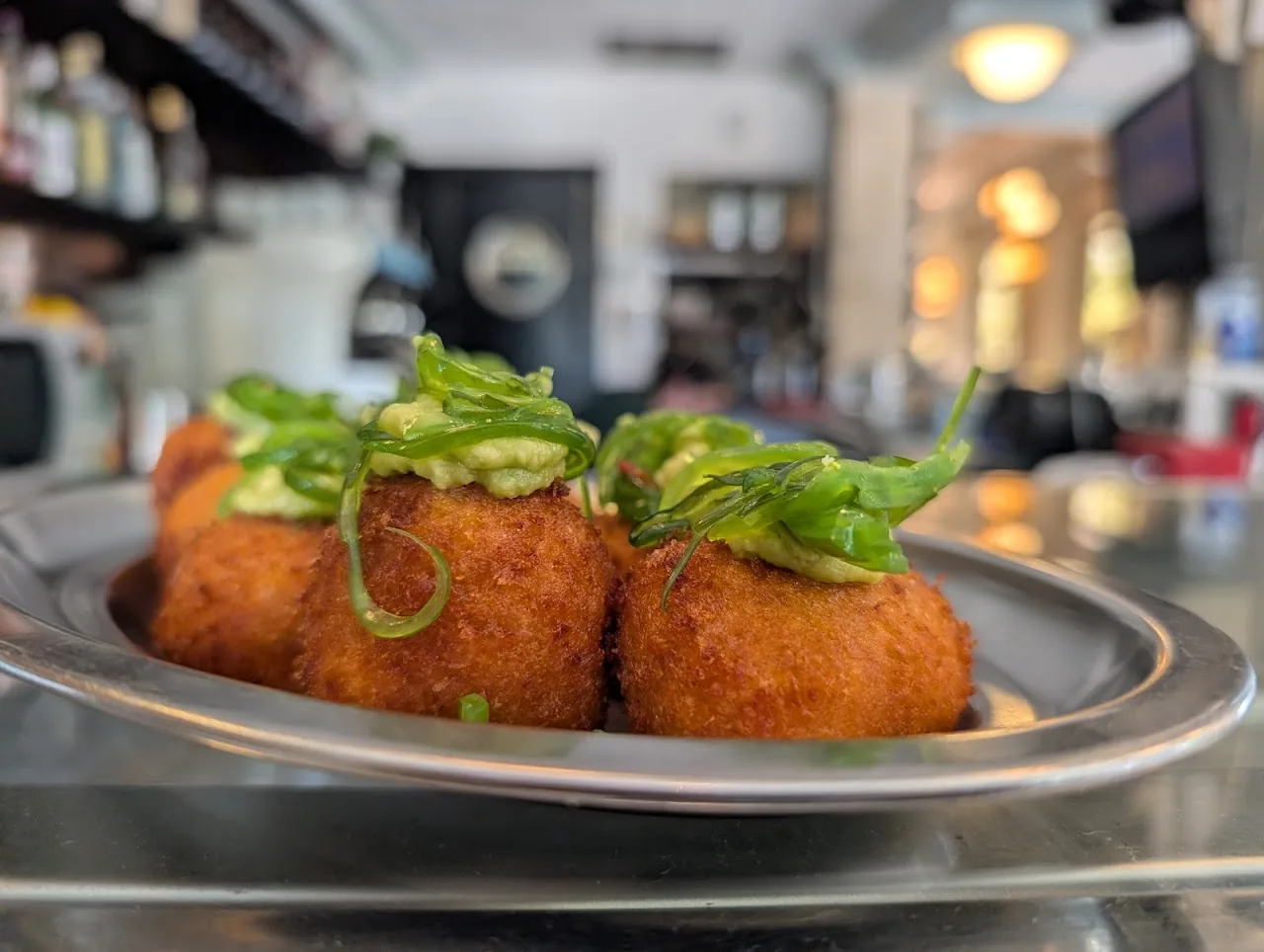 Fried croquettes topped with fresh greens on a metal plate