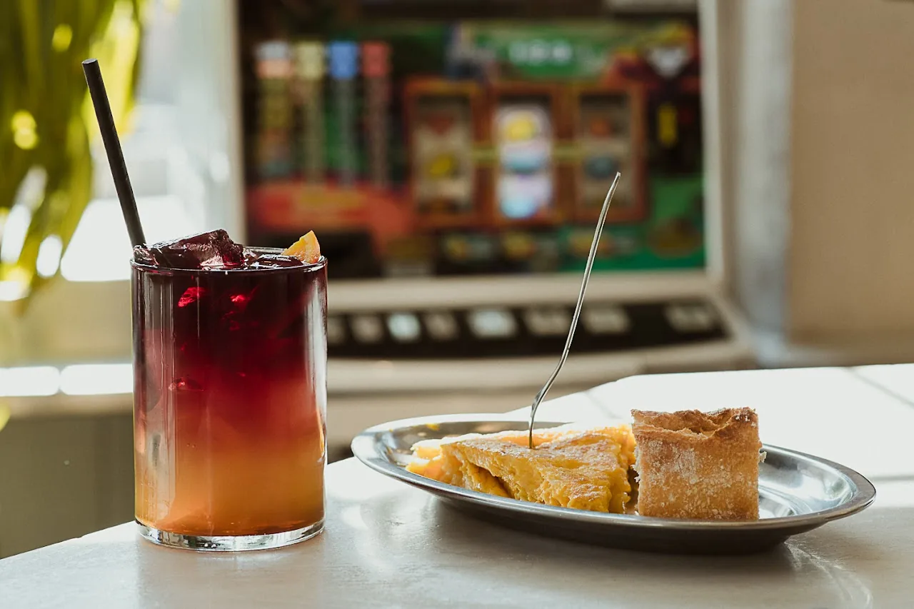 A red cocktail beside a small pastry on a plate